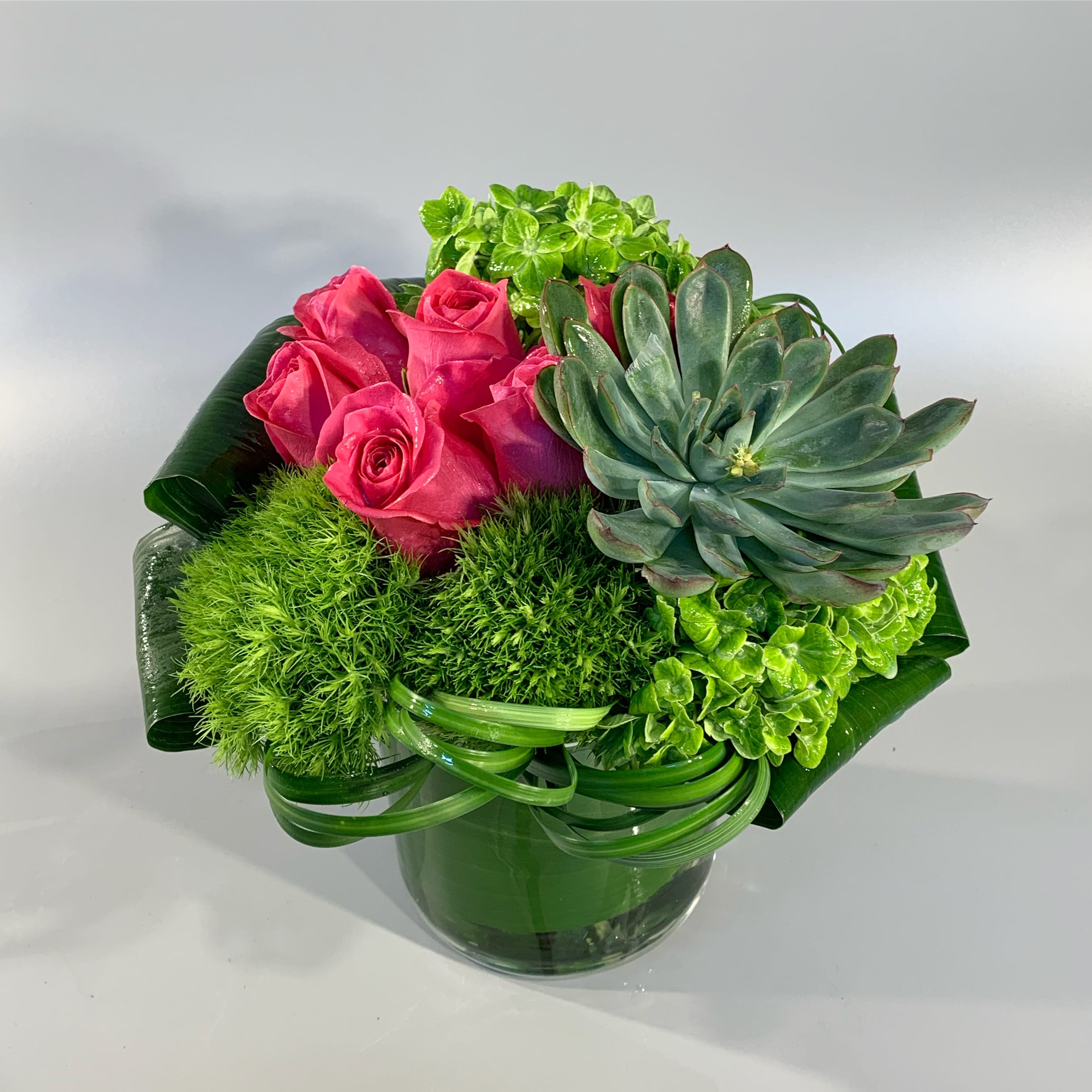 SWEET - Designed with vibrant roses, sculpted grasses, green hydrangea, sculpted leaves, a succulent floret hand-tied and placed in a clear glass vessel. 