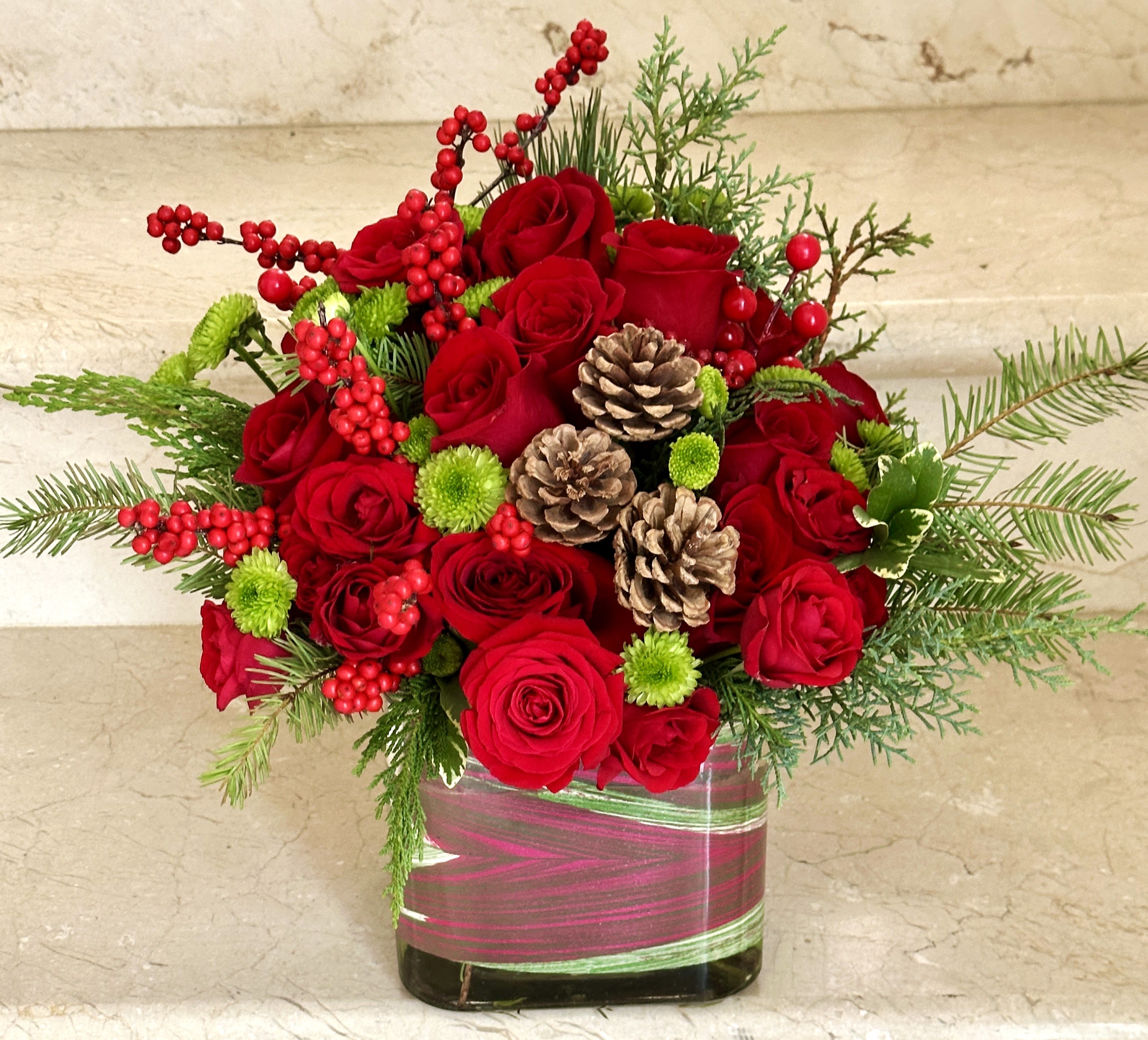 Christmas Delight - An elegant holiday arrangement featuring red roses in varying sizes, complemented by pine, pinecones, red berries, and festive Christmas decorations.
