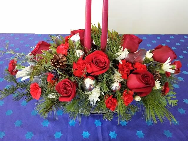 Elegant Christmas Centerpiece - Add a touch of festive charm to your holiday celebrations with this stunning Christmas centerpiece. Featuring vibrant red roses, red carnations, and lush pine branches, this arrangement is accented with holiday decorations like pinecones, ornaments, and delicate white flowers. Two elegant red taper candles complete the design, creating a warm and inviting ambiance for your dining table or holiday display.  Perfect as a gift or for your own seasonal decor, this centerpiece brings the spirit of Christmas to any setting.