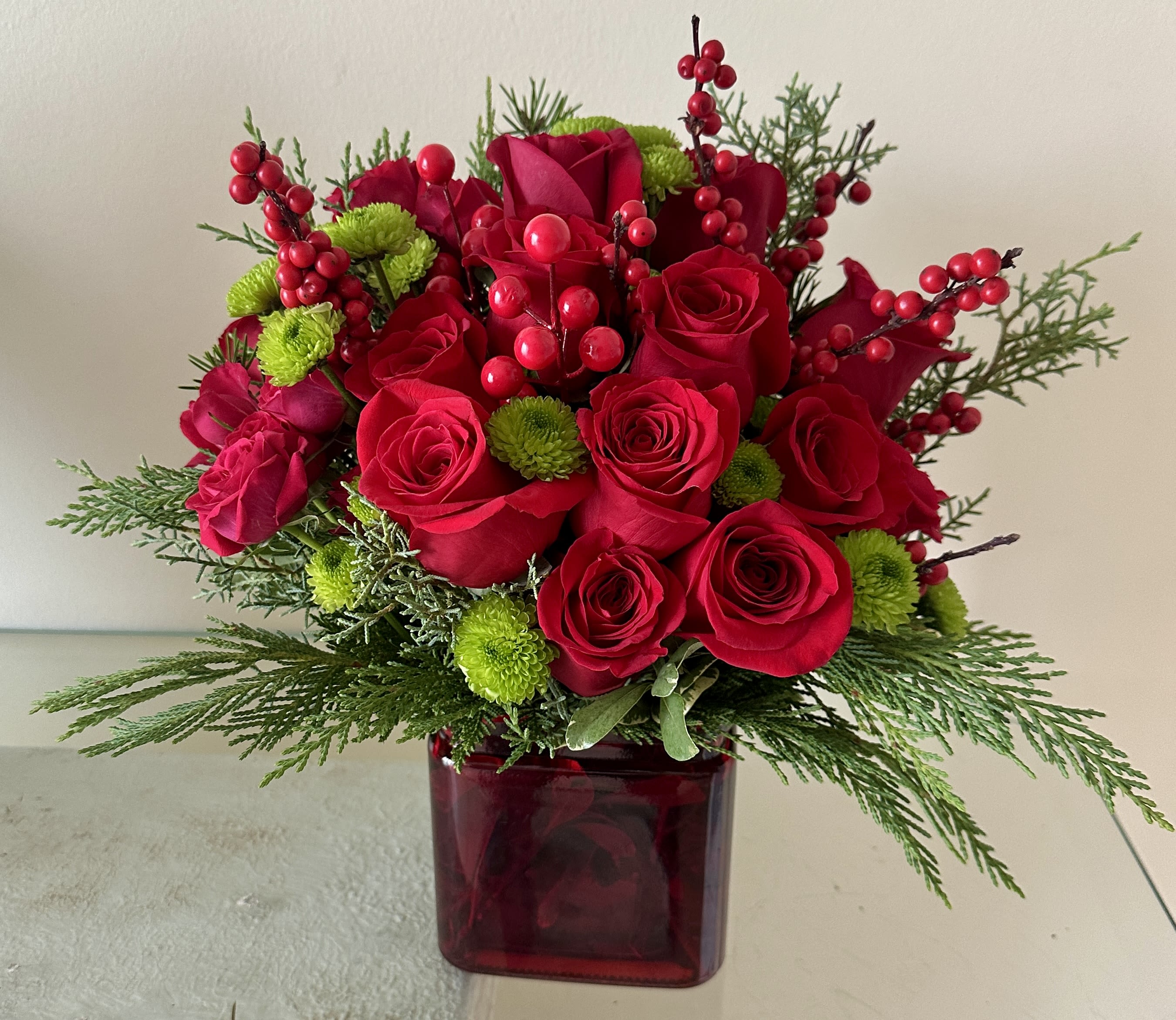 Joyous Holidays - A stunning holiday arrangement featuring vibrant red roses, green blooms, fresh pine, red berries, and festive decorations, perfect for the season.
