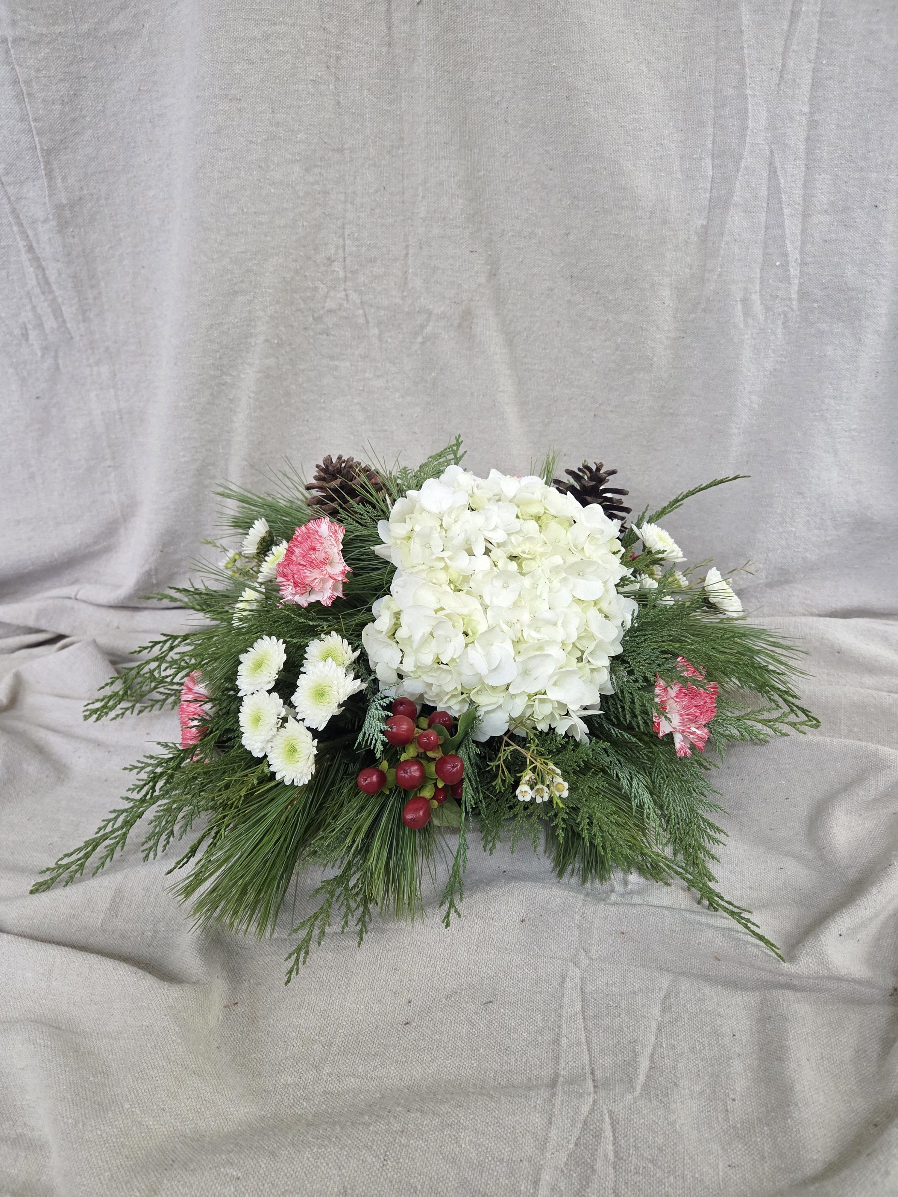 Snow and Berry Elegance Centerpiece  - Celebrate the season with this classic red and white Christmas centerpiece, beautifully accented with lush winter greens, rustic pinecones, and vibrant red berries. The rich, festive colors evoke holiday warmth and timeless elegance, while natural elements add a cozy woodland charm. Perfect for brightening your holiday table or gifting seasonal cheer, this arrangement brings the spirit of Christmas into any home with effortless style and joyful beauty.
