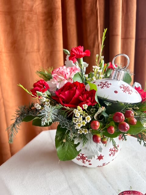 Peppermint Ornament Surprise - Add a joyful pop of Christmas cheer to any space with this festive ornament-inspired floral design. Nestled inside a decorative holiday ornament container, this piece features a charming mix of winter greens, white roses, seasonal mini carnations, berries, and delicate textural accents. Fresh evergreens and soft blooms come together to create a playful yet elegant arrangement perfect for gifting, decorating desks and counters, or bringing a touch of magic to your holiday celebrations.