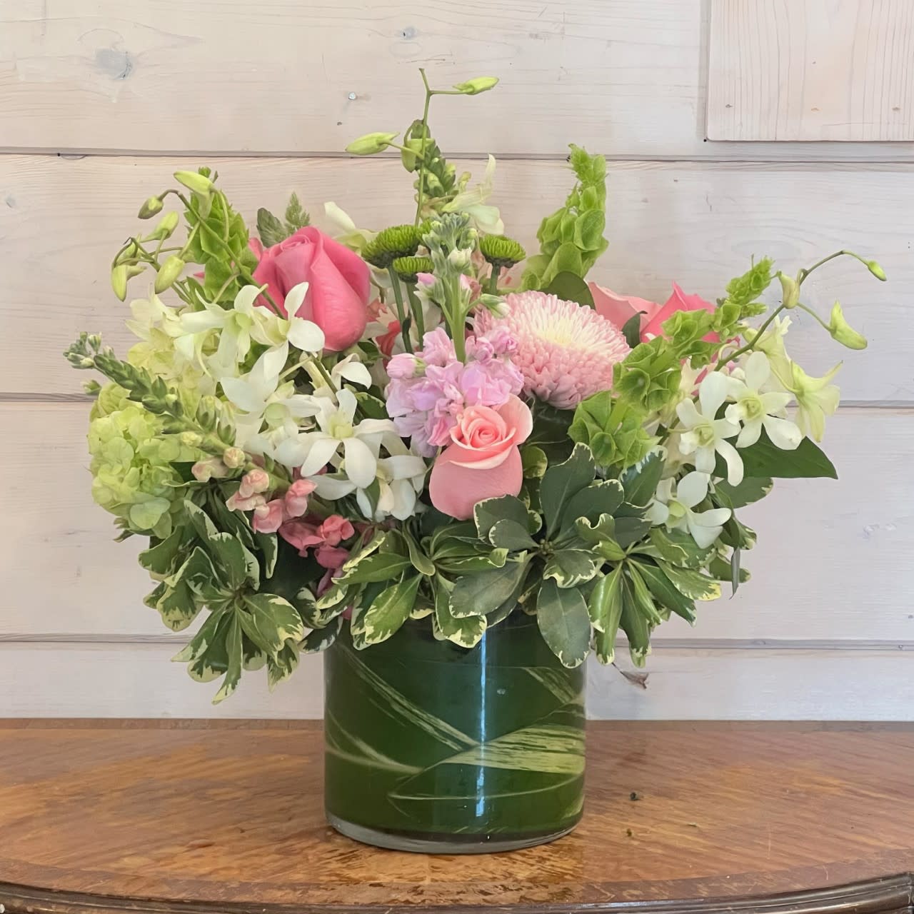 Boundless Love  - Green hydrangea, a mix of pink roses, snapdragons, chrysanthemums and stock, bells of Ireland, green buttons, and white orchids arranged in an extra large leaf lined round gather. approximately 16in tall and 16in wide. 