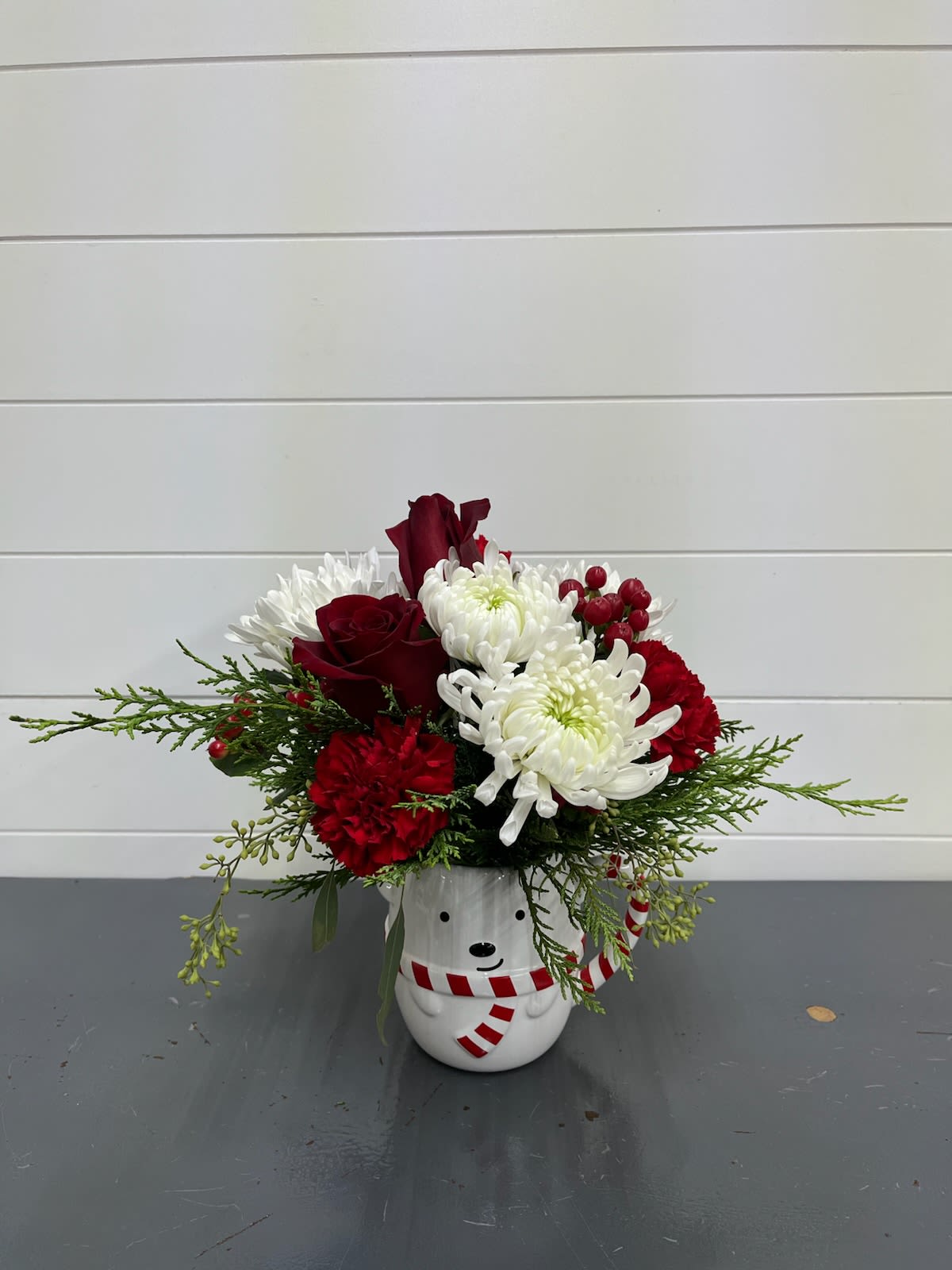Bear-y Merry - Bear-y Merry Bouquet The perfect dose of holiday cheer, all wrapped up in an adorable snow bear mug! This festive arrangement features a charming mix of fresh mums, cheerful carnations, and classic roses, accented with fragrant Christmas greenery for that cozy winter touch. Whether you’re sending warm wishes, decorating your own space, or gifting a little seasonal magic, this delightful design brings smiles, sweetness, and holiday spirit to any room. After the flowers fade, the snow bear mug makes a merry keepsake for hot cocoa all winter long!