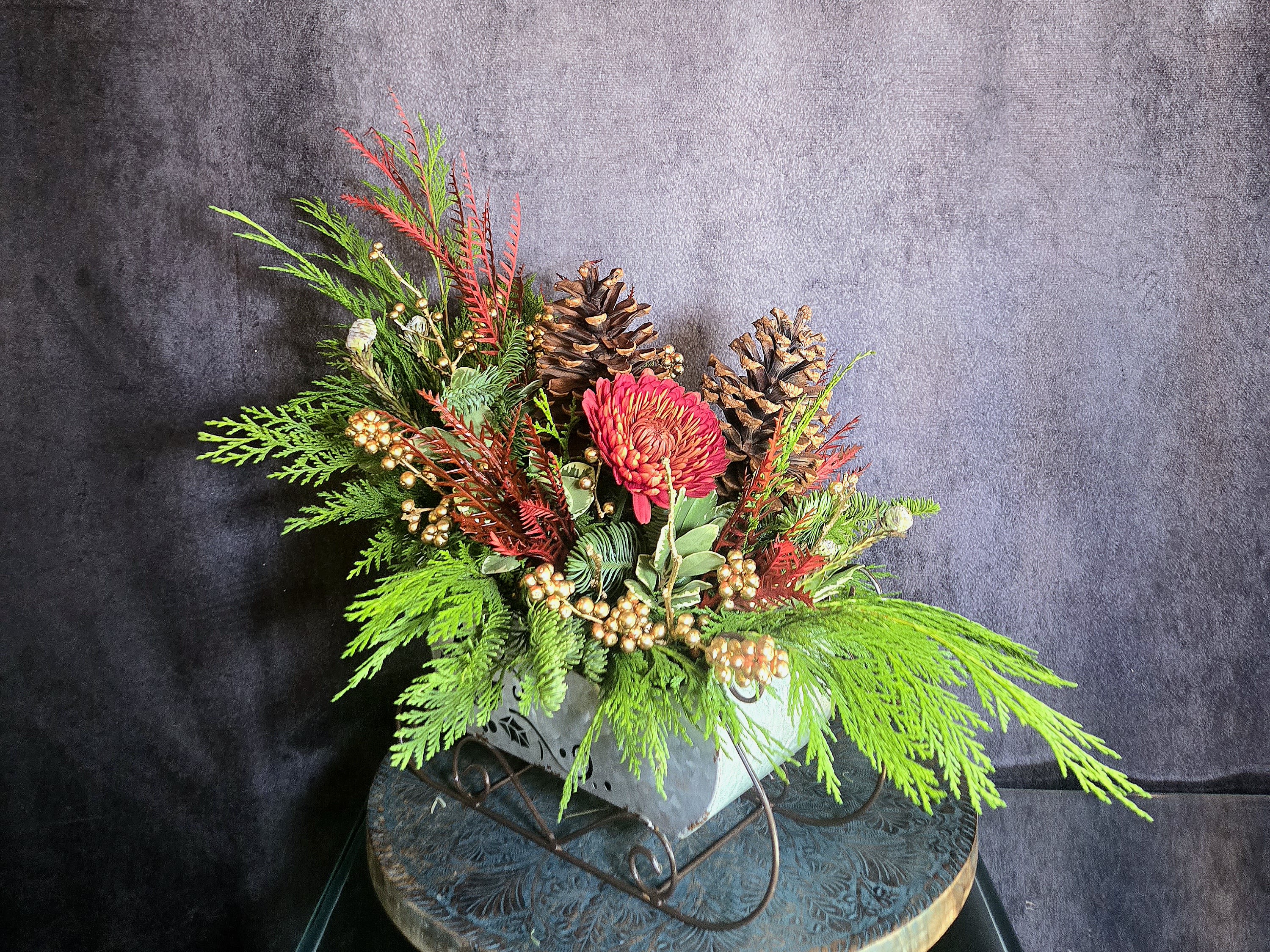 Sleigh Ride - Celebrate the Winter months with an evergreen &quot;Sleigh Ride&quot;, decorated with mums, winterberry, and pine cones, arranged in a beautiful sleigh container. This arrangement is the perfect gift to bring a touch of winter indoors and decorate a home or office space.