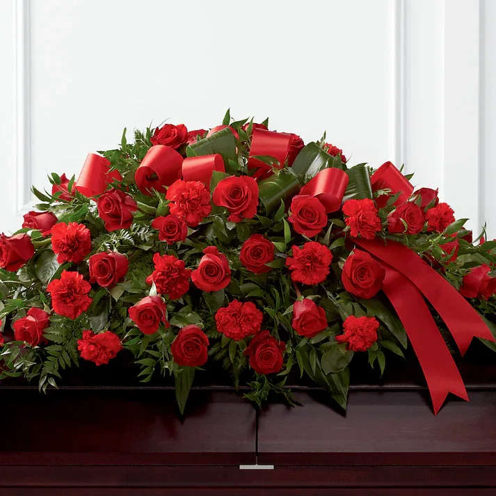 Tribute of Life Casket Spray - The Tribute of Life Casket Spray bursts with the love and passion that the deceased had for their life and loved ones. Rich red roses and carnations are gorgeously arranged amongst lush greens and accented with a red satin ribbon to create the ideal adornment for their casket at their final farewell service.  Details The Deluxe Spray is approximately 18"H x 40"W. Designed by florists, ready to display. Pet Safety Precautions: This bouquet or plant may include flowers and foliage that are known to be toxic to pets. To keep t