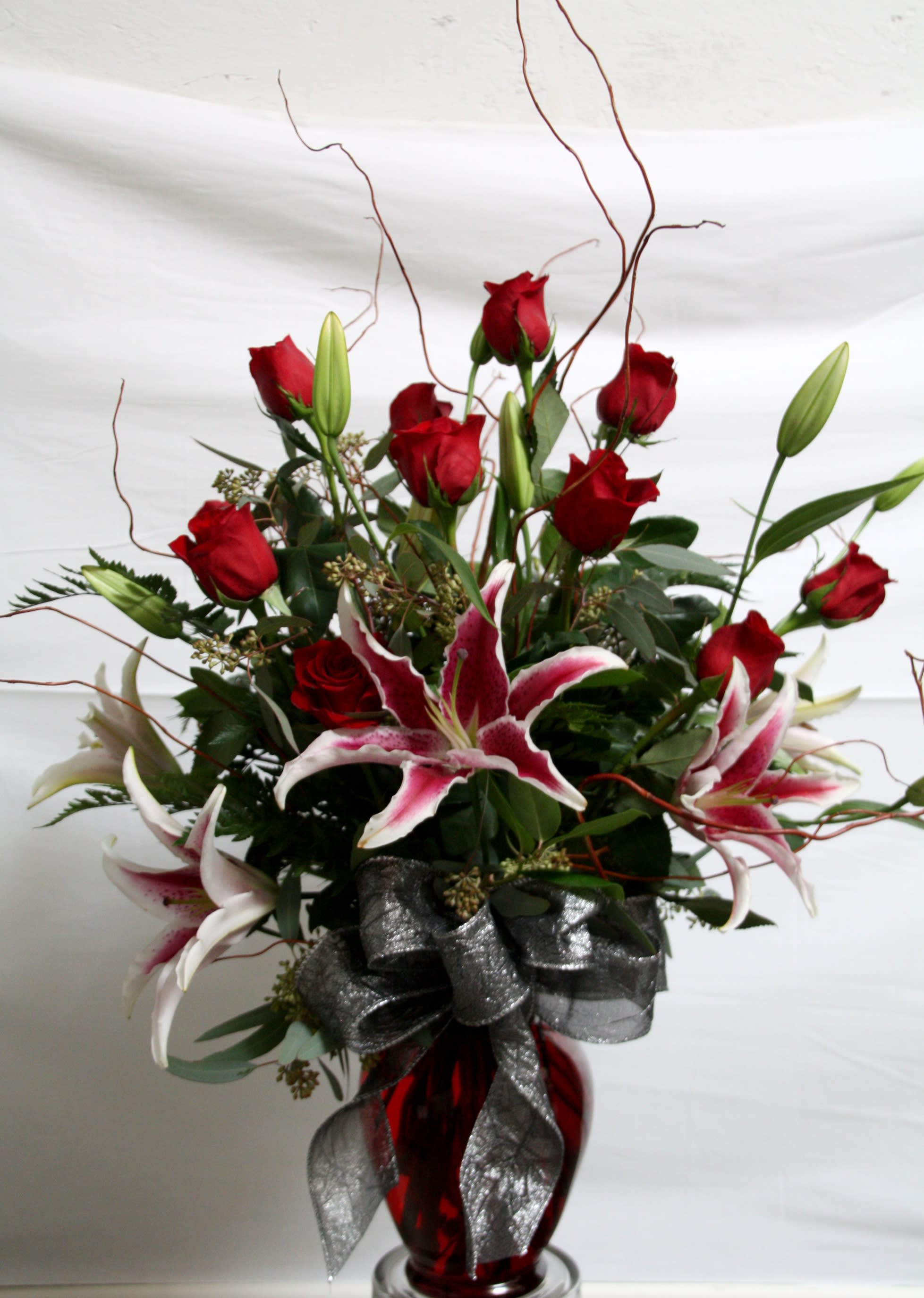 Classy Roses &amp; Lillies - This European style arrangement would be perfect for your classy woman. Gorgeous long stem red roses accompanied with fragrant stargazer lilies and accented with curly willow stems come in this complimentary red glass vase and complete with a large bow is sure to win her heart