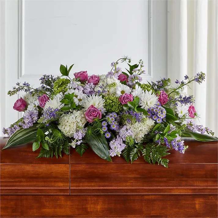 Meadows of Serenity Casket Spray - The Meadows of Serenity Casket Spray is designed using the calming aura of lavender hued florals, arranged by a local florist to adorn a casket with grace.  Details Spray is approximately 16"H x 40"W. Designed by florists, ready to display. Pet Safety Precautions: This bouquet or plant may include flowers and foliage that are known to be toxic to pets. To keep them safe, be sure to keep this arrangement out of your pet's reach.