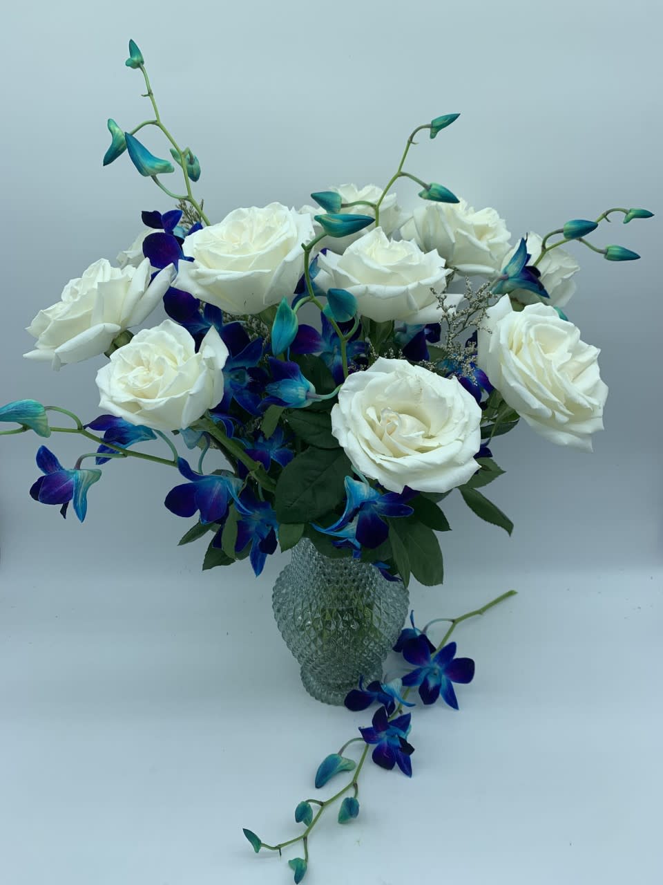   BLUE LAGOON $125/150/200 - Send a classic gift of love with this vase of one dozen long stem premium florist grade white roses and tropical dendrobium orchids in a blue keepsake vase.  Our upgrades include  additional roses and orchids to value.  PS: Don't forget to add a candle and some chocolates!