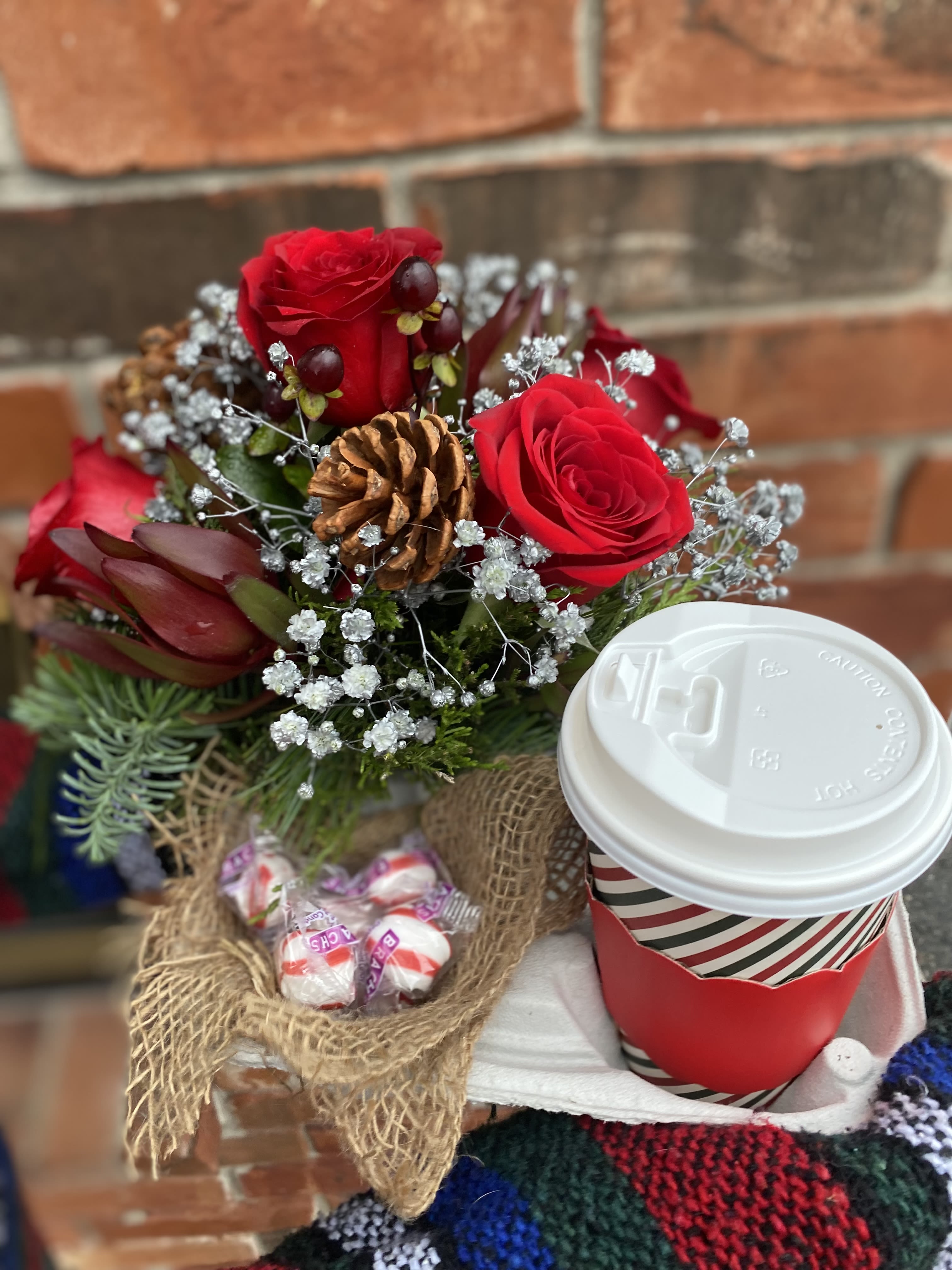 Holiday Cheer - Holiday Cheer is a joyful and festive flower arrangement bursting with classic Christmas charm. Bright red blooms—such as roses, carnations, or holiday mums—are paired with fresh winter greens, pinecones, and seasonal accents for a warm, welcoming look. We can provide the beverage of coffee or hot chocolate choices in special instructions.