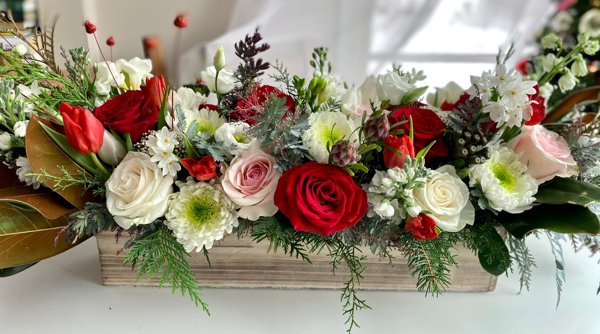 Symphony of Holiday Joy - This Holiday centerpiece is the symphony of Holiday joy! Filled with fresh premium flowers such as roses, lisianthus, spray roses, ranunculus, and winter greens. A true Holiday magic on a table! Comes arranged in a wooden box.  "In the symphony of holiday joy, each note is a shared smile, and every gathering is a chorus of love."    