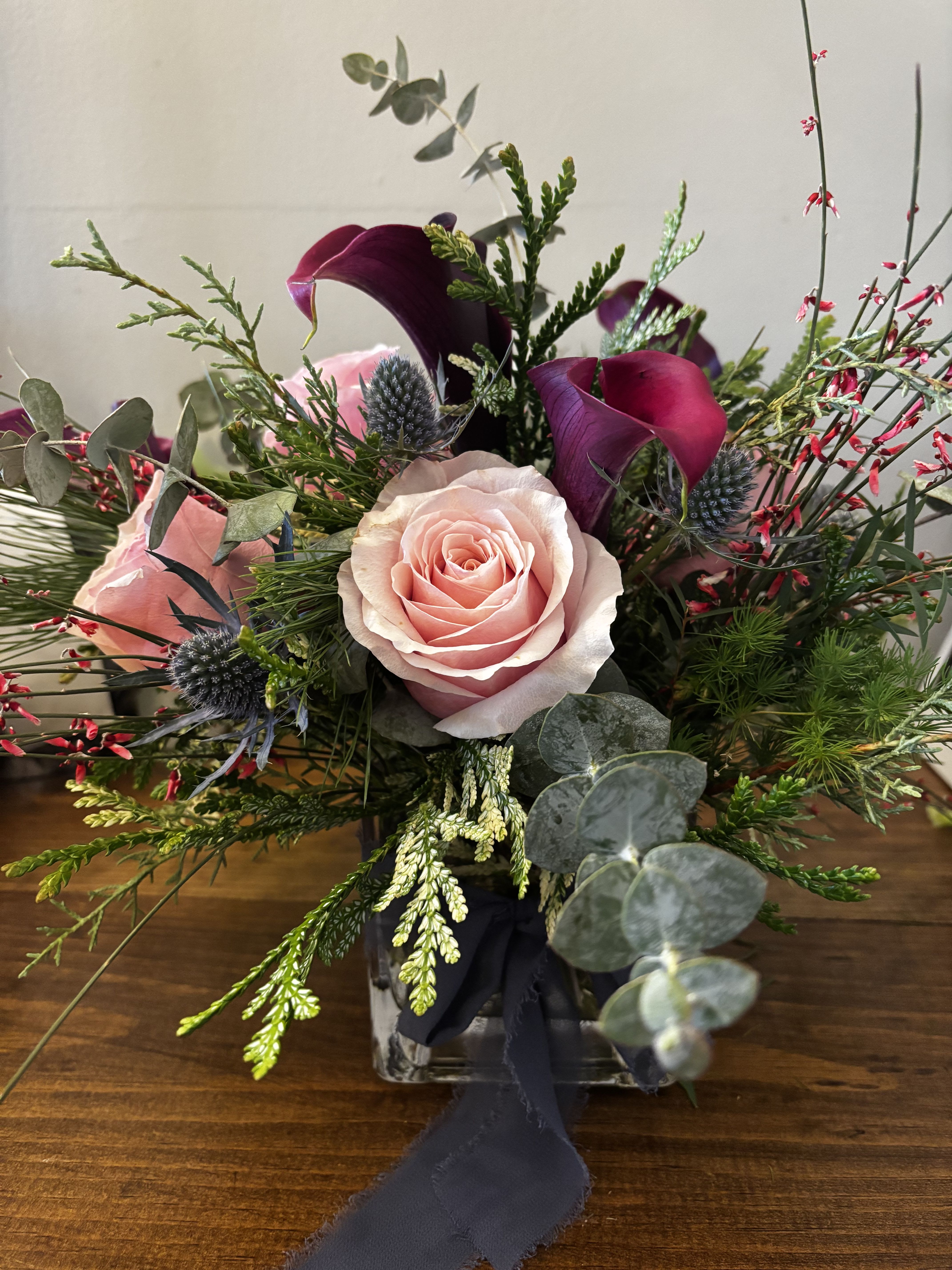 Winter Charm  - Our Winter Charm centerpiece has a touch of holiday magic and color to sure wow your family and friends this holiday season.  A mix of evergreens, eucalyptus, pink and berry colored blooms all housed in a vase. 