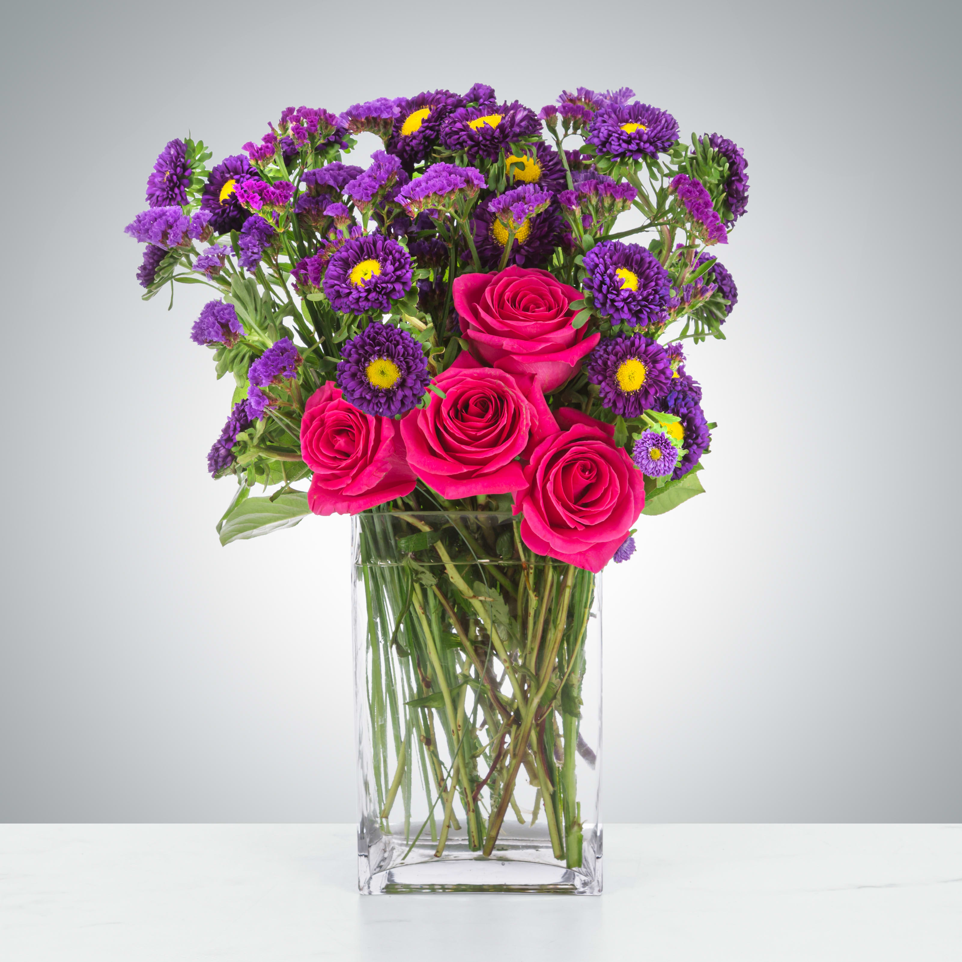 Twilight Glow by BloomNation™ - This pink and purple arrangement is tough! Purple Matsumoto asters, purple statice, and hot pink roses are all sturdy flowers and will provide your recipient with a fresh-looking arrangement for a long time. A good option to send for celebrating a birthday, a graduation or just because.  Approximate Dimensions: 14"D x 18"H