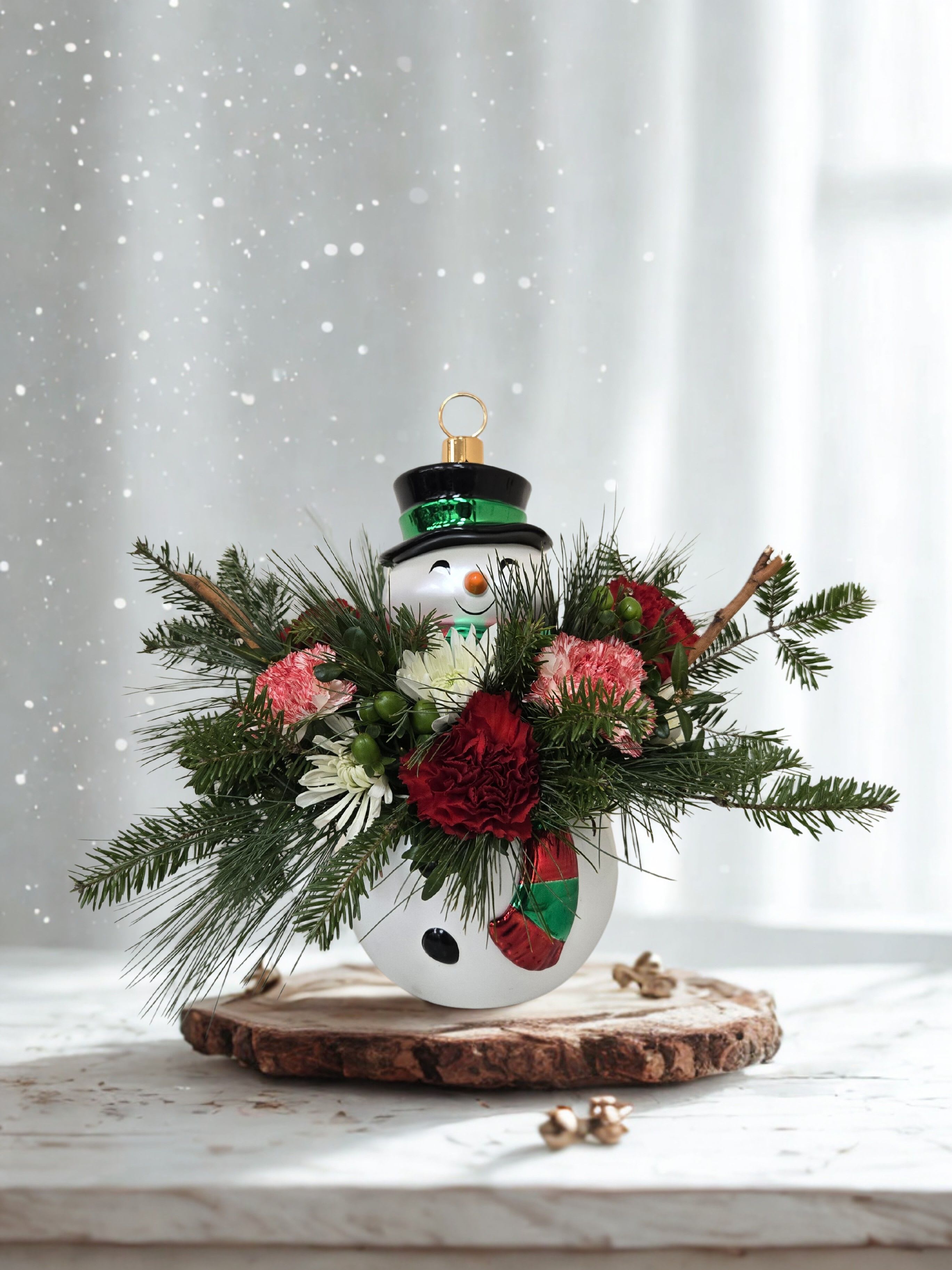 Snowman - Celebrate the season with our charming Snowman Christmas Arrangement, a festive holiday design created in an adorable reusable snowman container. This handcrafted arrangement features fresh seasonal blooms and winter greenery arranged in a playful, cheerful style—perfect for adding holiday joy to any home, office, or gift delivery.  Each piece is uniquely designed by our floral team, ensuring your Christmas flower arrangement feels fresh, festive, and one-of-a-kind. When the flowers have faded, the snowman container can be enjoyed long after the holidays as a decorative accent, candy dish, small planter, or keepsake you can bring out year after year.  Ideal for holiday gifting, seasonal décor, winter birthdays, or sending Christmas cheer, this arrangement is available for same-day flower delivery in Warrington, PA, and surrounding areas.  A fun, heartwarming Christmas flower gift that’s guaranteed to make anyone smile.