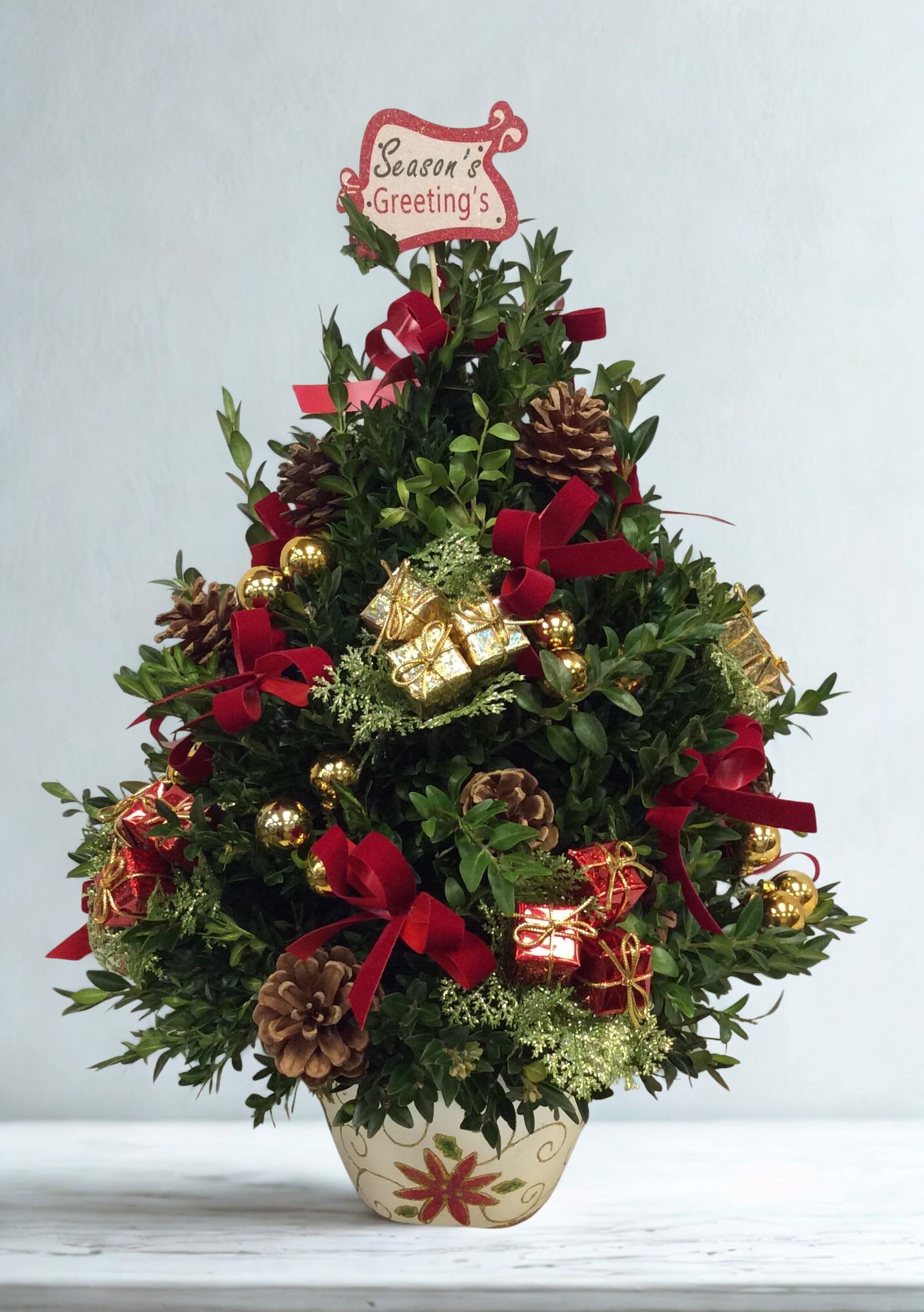 Mini Christmas Tree - Add festive cheer to any space with our handcrafted Mini Christmas Tree Arrangement, a charming tabletop holiday design created with fresh seasonal greens. Each tree is thoughtfully decorated in a classic Christmas style, with accents chosen by our designers based on availability, ensuring every piece is unique while keeping the same warm, festive look.  Perfect for homes, offices, apartments, nursing homes, or holiday gifting, this compact tree brings the spirit of Christmas to any room—no large decorating required. Its size makes it ideal for desks, countertops, entry tables, or small holiday displays.  Presented in a decorative holiday container and topped with a cheerful seasonal message, this tabletop Christmas tree is designed to last throughout the holiday season and bring joy wherever it’s placed. Available for same-day Christmas delivery in Warrington, PA, and surrounding areas.  A delightful and long-lasting Christmas gift arrangement that spreads holiday magic all season long.