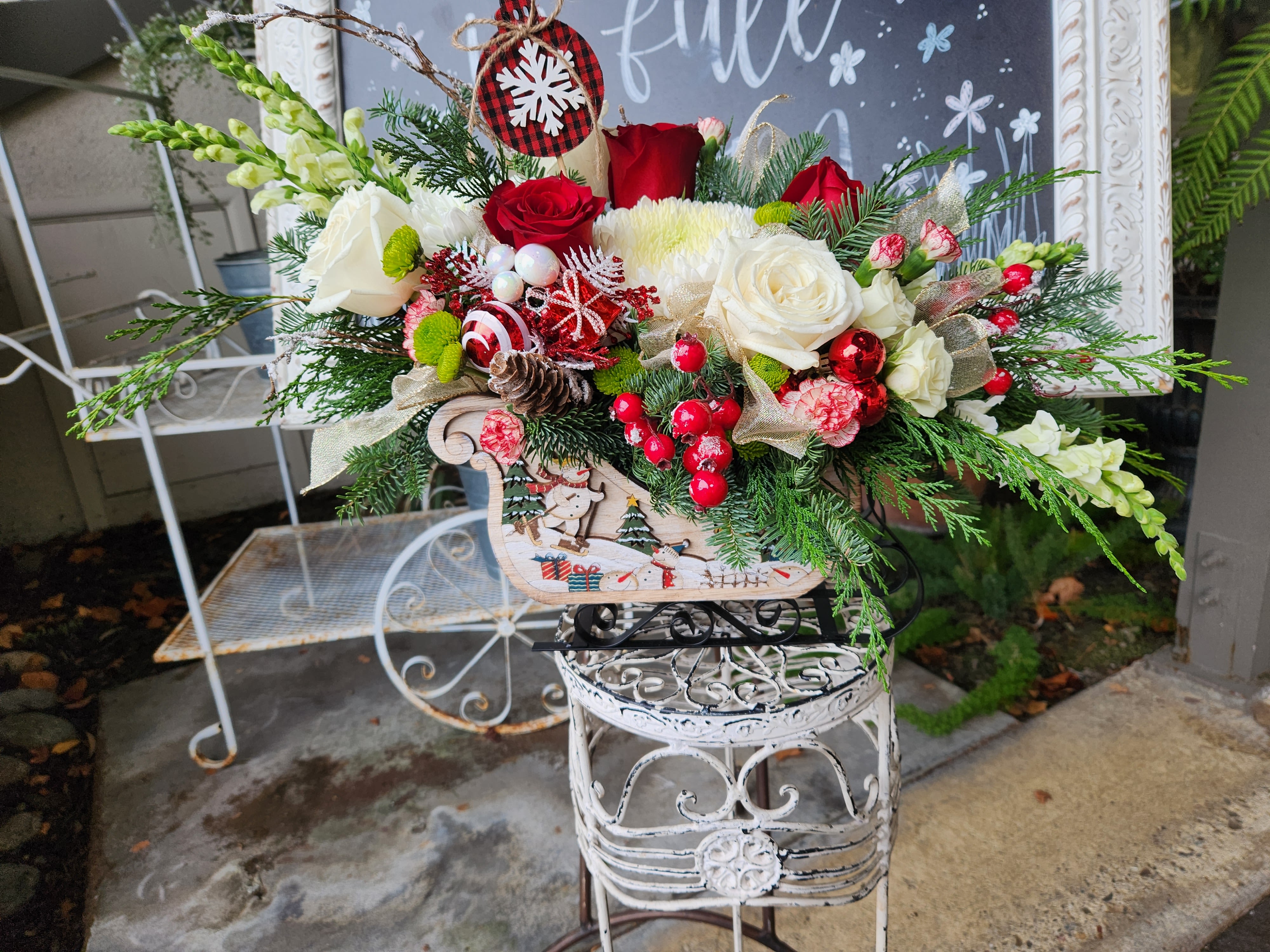 Rustic Snowman Sleigh Arrangement   - A beautiful rustic snowman sleigh designed with lots of winter evergreens red and white roses, spray roses, carnations holiday berries and lots of ribbons. This piece is fun and will look beautiful in any cozy home. Happy Holidays  pictured is deluxe size 