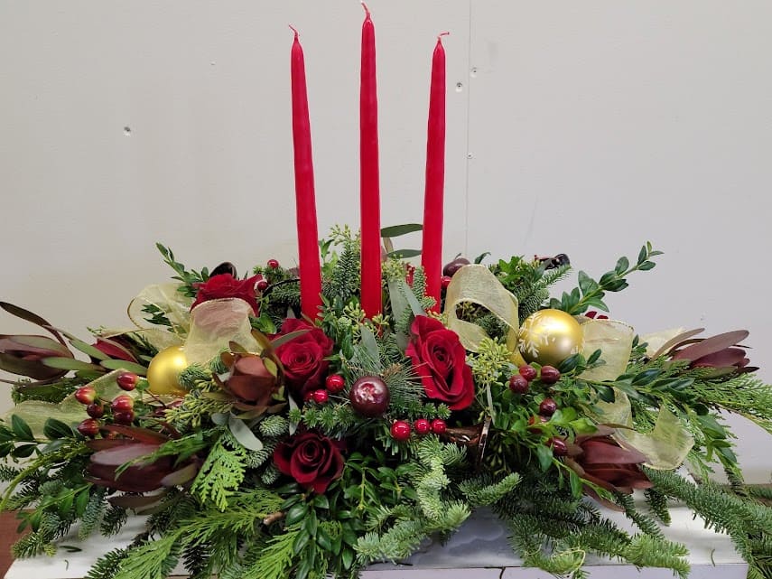 Three Candle Centerpiece - Traditional long and low arrangement that includes a fresh beautiful assortment of evergreens. Includes, roses, berries and tropical flowers. Gold and red accents included. Please include instructions for special requests. Example, ( silver rather then gold). For questions call us at 410-638-6300.