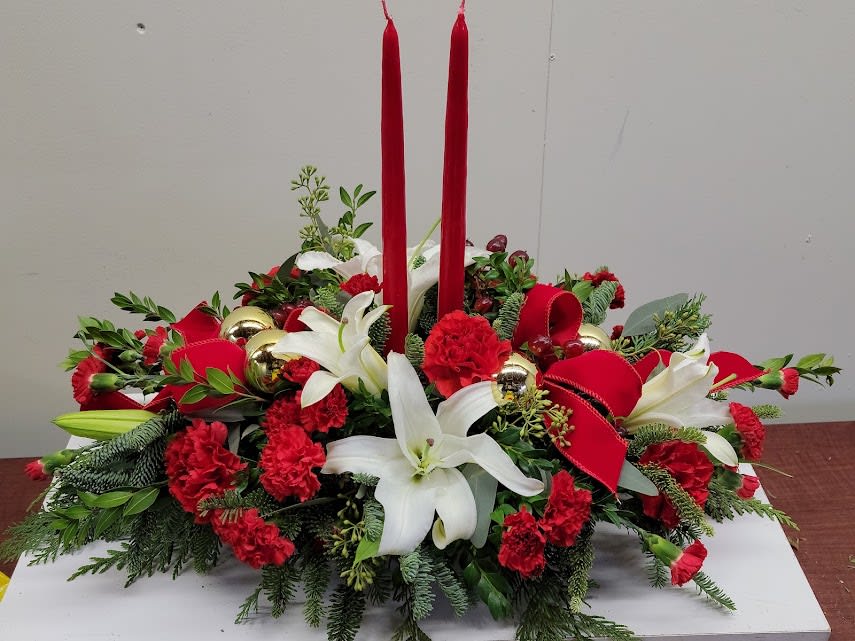 Two Candle Centerpiece - Traditional long and low centerpiece, includes red carnations, red mini carnations ad white lilies. Standard size shown. Deluxe and Premium will also include red roses. Red candles and red bows are also included unless other colors are requested. For questions please call us at 410-638-6300.