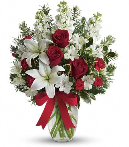 Holiday Snowflakes - Snowy white lilies, red roses and carnations complemented with fragrant white stock - truly a gift for the senses. A charming choice for a birthday, anniversary, hostess gift or any special occasion. Also a great gift &quot;just because.&quot; The cheerful arrangement includes red roses, white a lilies, white alstroemeria, red miniature carnations and white stock accented with holly, noble fir and a red satin ribbon.   Orientation: One-Sided 21&quot; H x 16&quot; W
