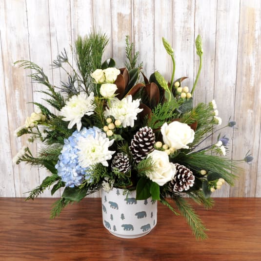 Grizzly Bear Hugs - Large keepsake bear container, filled with wintery neutral blooms in blue and white with pinecones and wintergreens. Larger version of Polar Bear Hugs. 
