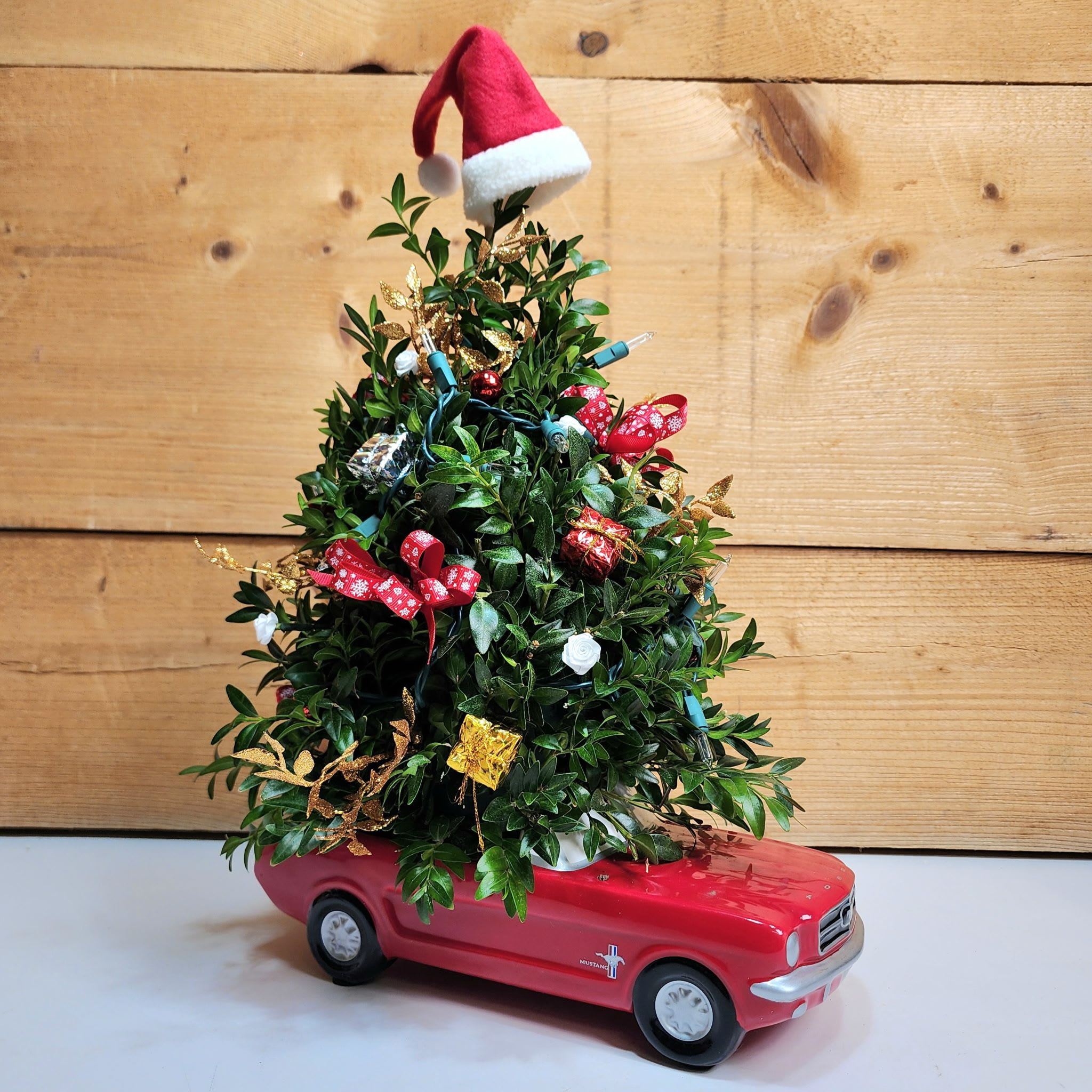 Run Run Rudolph - Santa's gotta make it to town, and he's doing it in style with our Run Run Rudolph arrangement! This fun arrangement features one of our best selling Boxwood Trees being transported in a classic Red Mustang, making this the perfect gift for someone who wants holiday decor with a fun twist!  Dimensions approx. L 10&quot; x H 18&quot;  NOTE: Decorations may vary based on availability, but will be kept as close as possible to the images provided