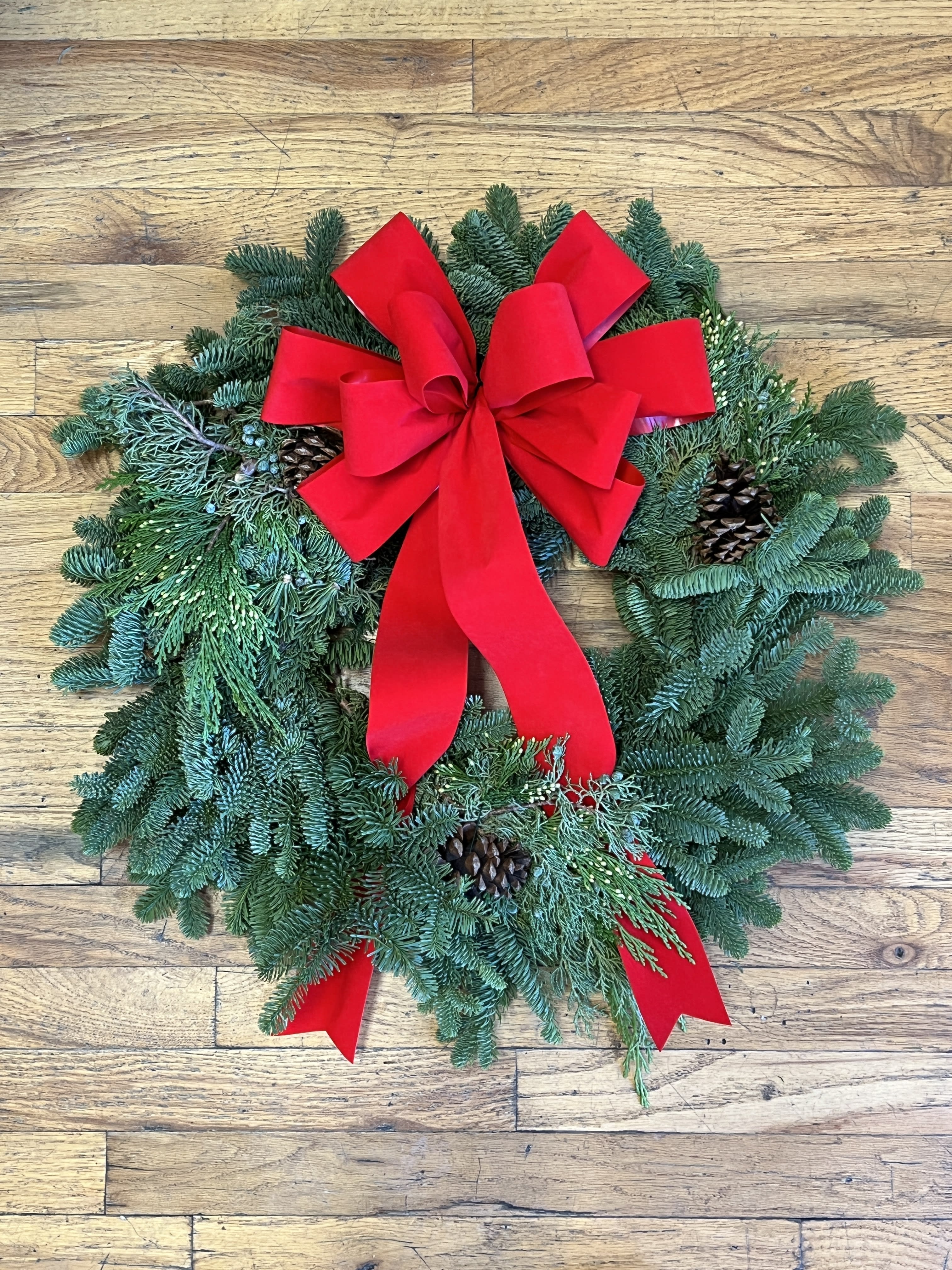HLD-03 - Fresh Mixed Evergreen Wreath Accented With Pinecones and a Hand Tied Red Bow. 