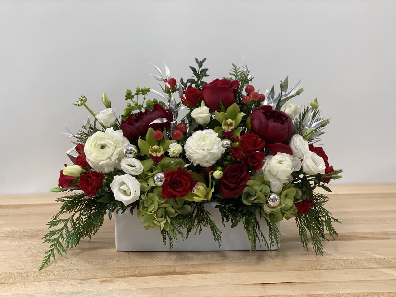 Happy holidays - A combination of peonies, ranunculus, cymbidium orchids and roses, in a white ceramic container makes this arrangement a classy, cheerful and elegant Christmas centerpiece. 