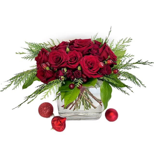 Crimson Noel - Crimson Noel is a contemporary symphony of passion and nature. This exquisite arrangement features the rich allure of deep red roses and spray roses, intertwined with the lush beauty of evergreen foliage and crimson berries. A harmonious dance of elegance and natural charm, this bouquet is a celebration of tradition and sophistication- designed in a clear glass vase. 