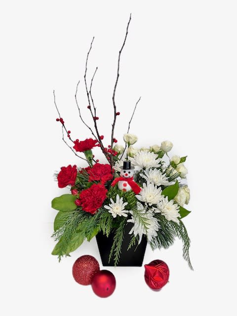 Frosty's Favorite - Meet 'Frosty's Favorite'—where timeless beauty meets holiday whimsy! This enchanting arrangement, dressed in classic red and white, boasts long-lasting blooms like mums, carnations, and spray roses, that capture the essence of lasting tradition; while a striking branch of ilex berries brings a unique touch. A winter wonderland brought to life in flowers, accented by a delightful little snowman nestled among the petals. Embrace the season with this merry blend of enduring elegance and playful holiday spirit!