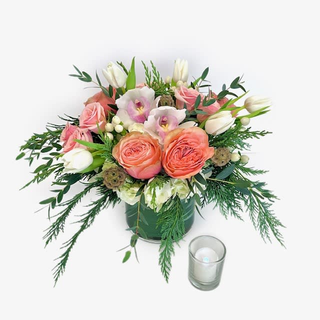 Peach Frost - Step into warm winter wonder with our Peach Frost bouquet! Delicately curated with a blend of pristine white and soft peach blooms, this arrangement embodies the subtle beauty of the season; featuring a PJs favorite, peach Kahala roses, lush white hydrangea, long lasting white cymbidium orchids, and classic tulips. Adorned with a touch of frost-inspired glamour, it's a stunning symphony of elegance and holiday charm. Perfect for adding a frosty, yet warm, touch to any festive décor. Bring the enchantment of winter indoors with our exquisite Peach Frost bouquet. Designed in a leaf lined, clear glass cylinder. Accented with mixed evergreen and fragrant eucalyptus.