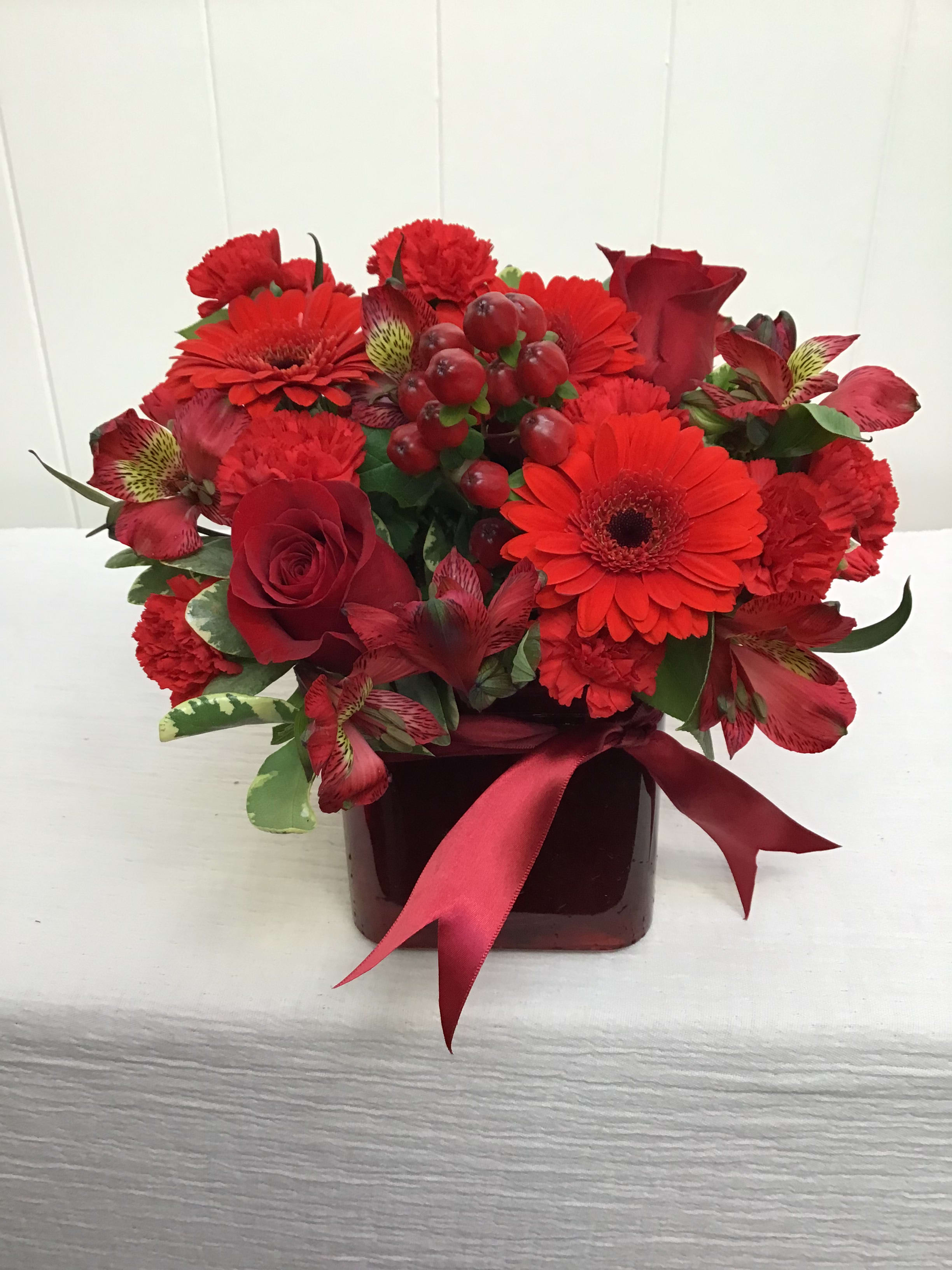 Classic Red - An all-red arrangement in a colored cube, featuring a variety of red flowers such as roses, berries, alstroemeria, and gerbera daisies. 