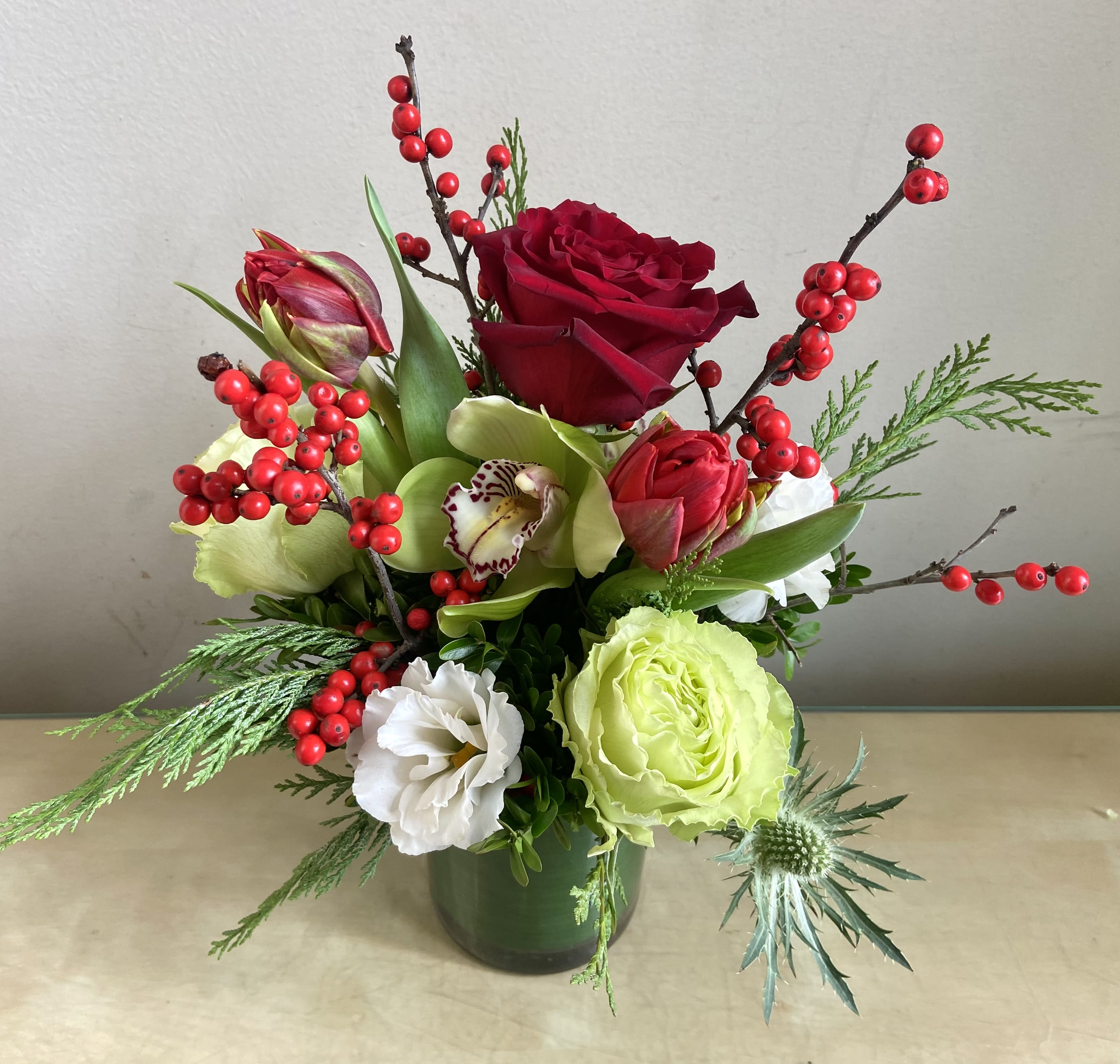 Holiday Cheer - Cheerful holiday red, white and green arrangement with roses, lisianthus, cymbidium orchids, ilex berries &amp; winter greens.