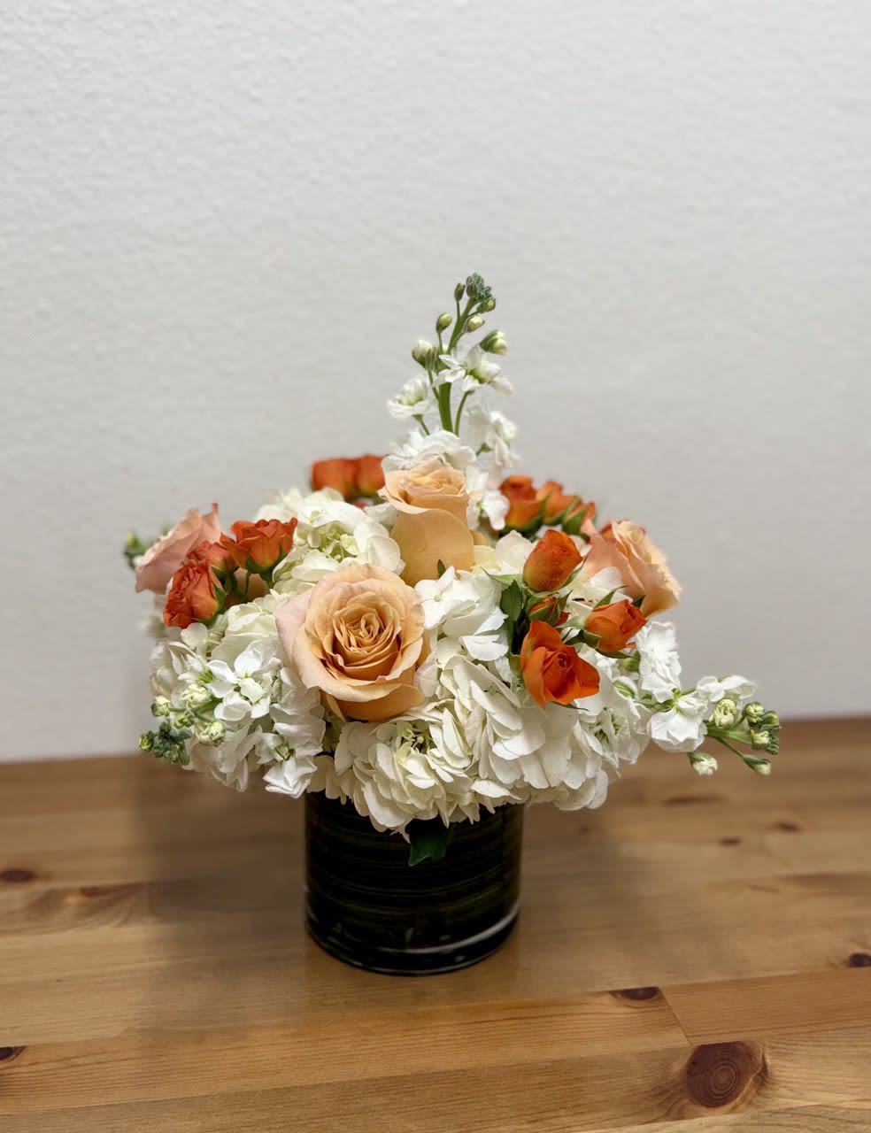 Papaya - Gorgeous flower arrangement made in a cylinder vase, a fabulous way to celebrate any occasion This beautiful vase is arranged with white hydrangea, white stocks, light peach shimmer roses, and orange spray roses.