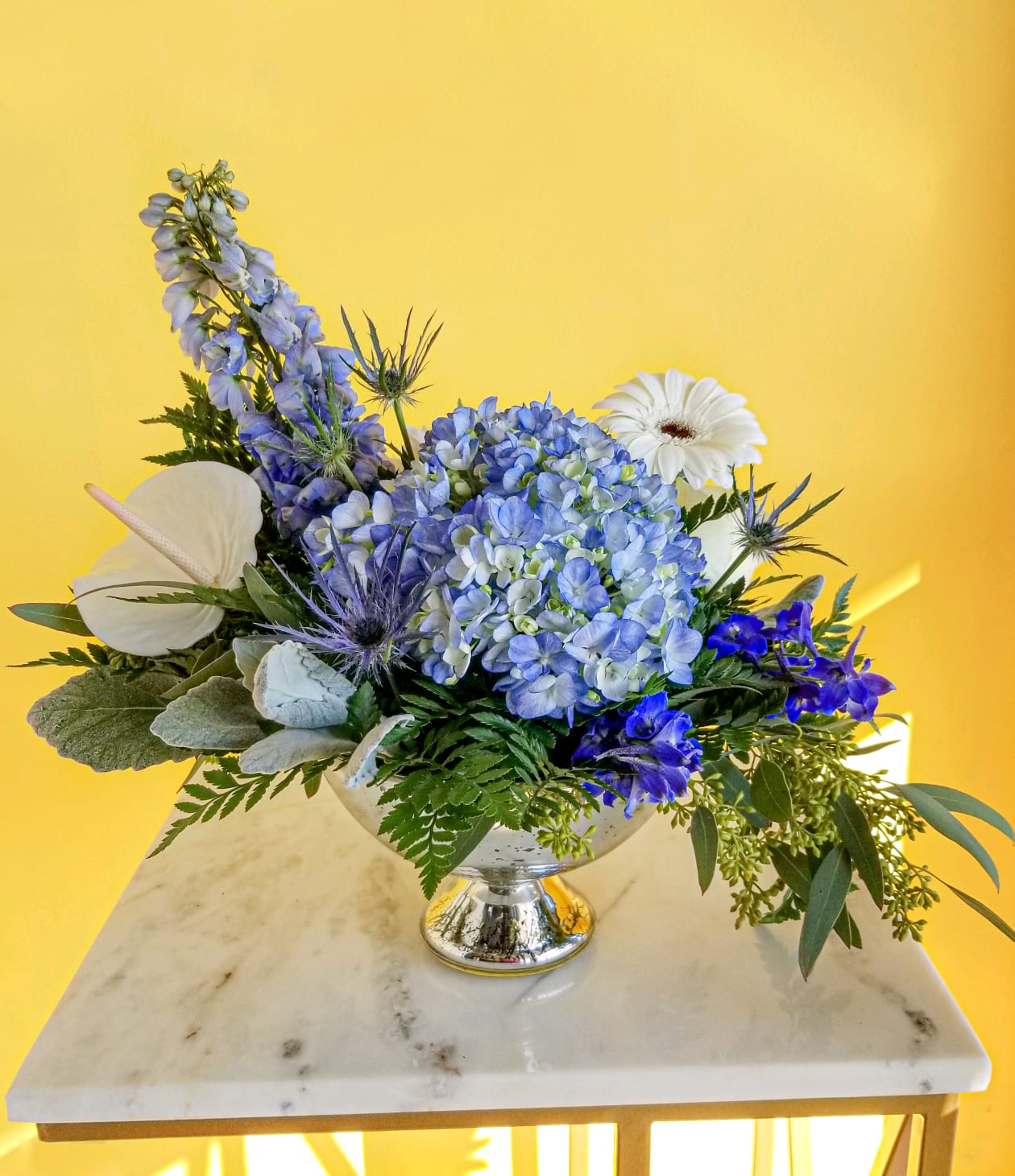 Midnight Snowfall - This dreamy blend of fresh blue and white flowers in a mercury pedestal dish is a sign of a wondrous season! It's a bright gift for Hannukah or a pretty, petite floral arrangement for any wintry day.