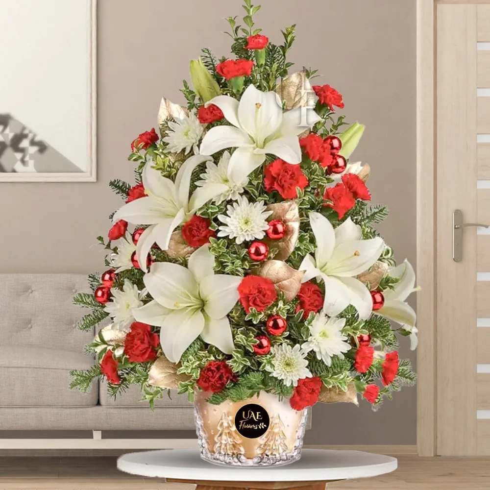 Enchanting Christmas Tree  - Illuminate the holiday spirit with our enchanting Christmas tree-inspired arrangement. Crafted with care, it boasts white lilies, red carnations, and white chrysanthemums, accentuated by golden sprayed leaves and vibrant red Christmas balls. the perfect centerpiece for festive gatherings or a heartfelt gift to spread joy and warmth during the holiday season.