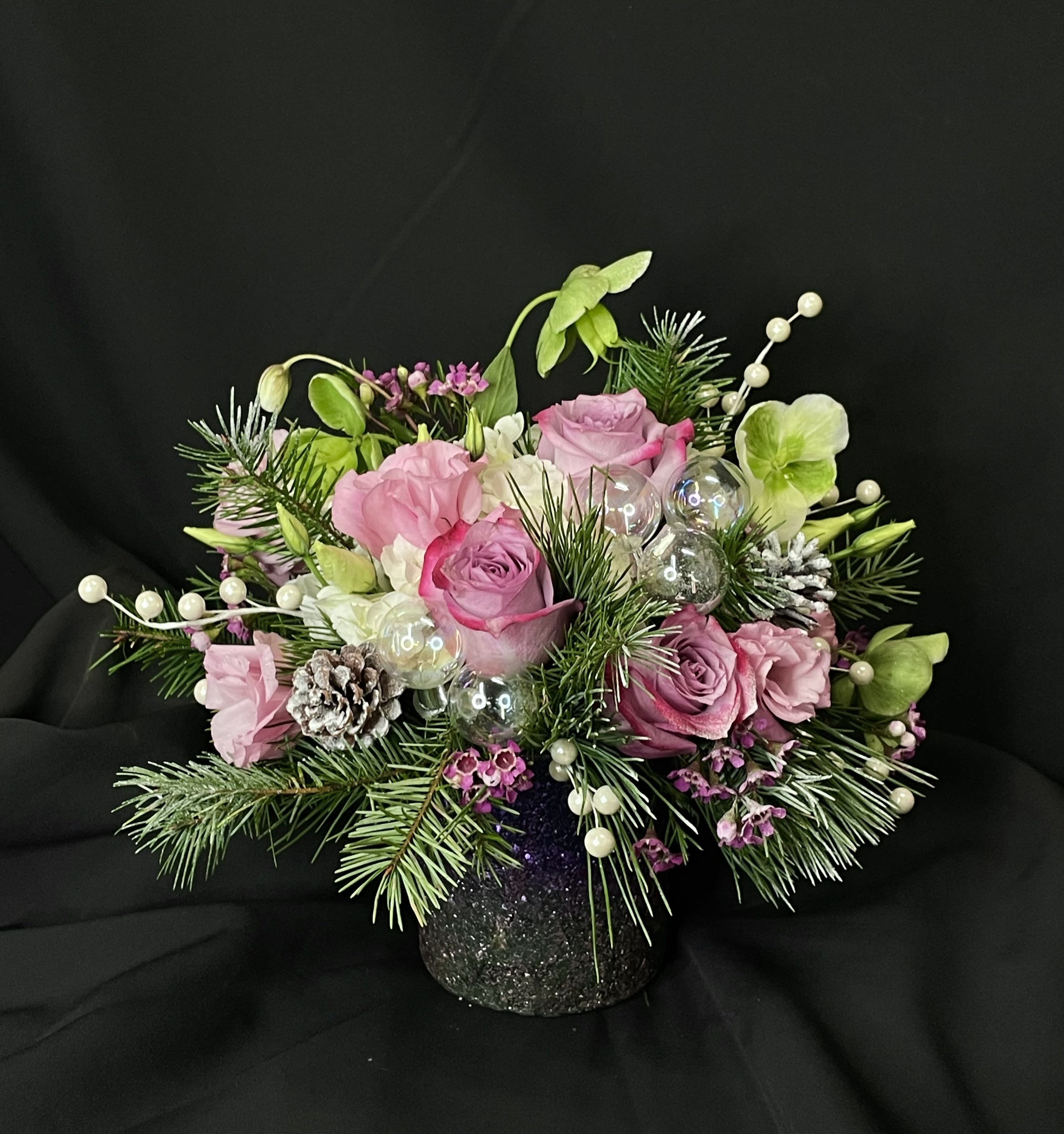 Sugar Plum Fairy - Love the holidays but red's not your favorite? Meet Sugar Plum Fairy, a pink and purple arrangement in a festive sparkly container reminiscent of the Nutcracker's most special character. Perfect for anyone who wants to a little unique pep to their Christmas flowers. Along with roses, heliboris and lisianthus, this arrangement features, pine, pinecones, pearly berries, and iridescent ornaments.