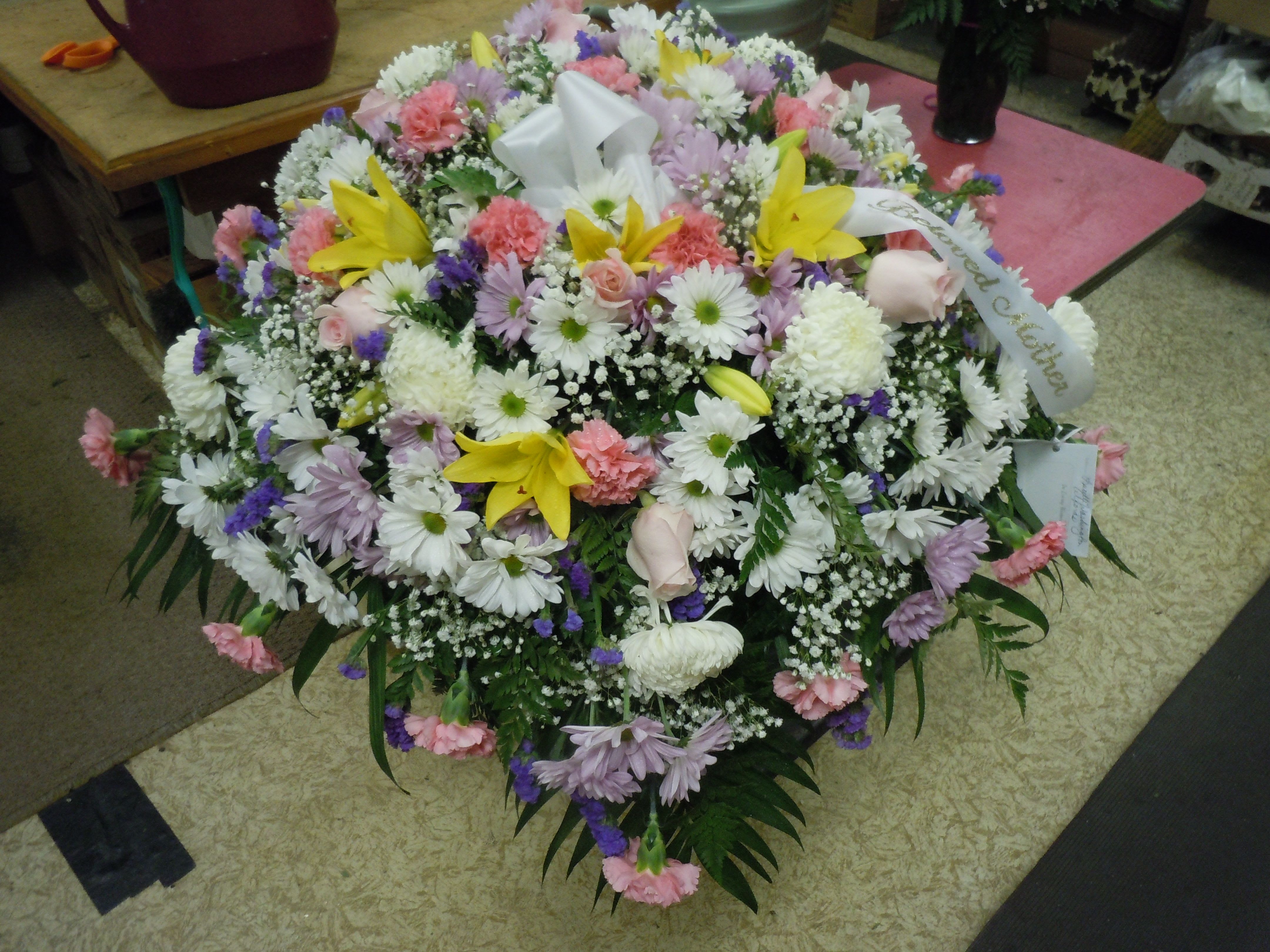 C15 Casket Spray - A mixture of white fuji mums, pink roses, pink carnations, white and lavender daisies, purple statice, yellow lilies, greens, and baby's breath.    Banner - $15.00 + extra  Substitutions may apply, pending flower availability.