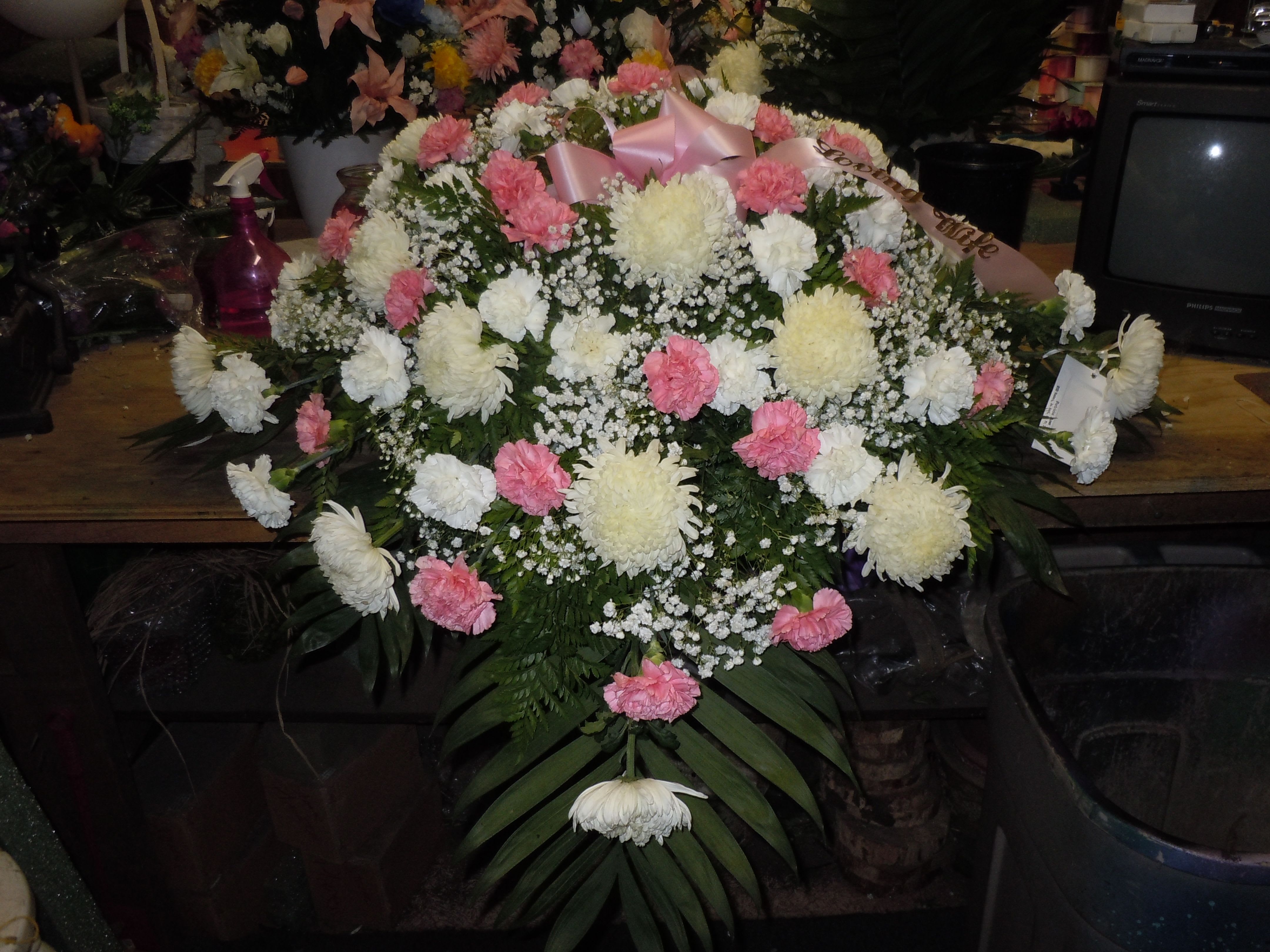 C16 Casket Spray - A mixture of white fuji mums, pink and white carnations, greens, and baby's breath.    Banner - $15.00 + extra . Substitutions may apply, pending flower availability.