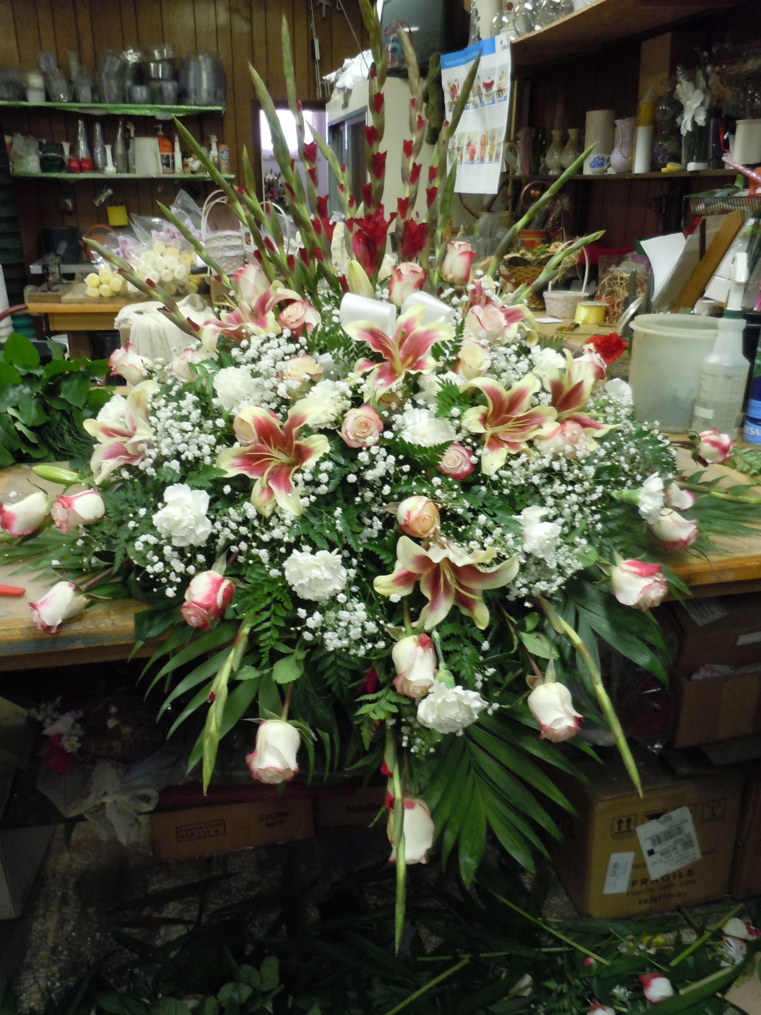 C24 Casket Spray - includes burgandy tipped roses , shocking lilis, gladiolas, baby's breath and      greens. includes bow.  Banner - $15.00 + extra  Substitutions may apply due to flower availability