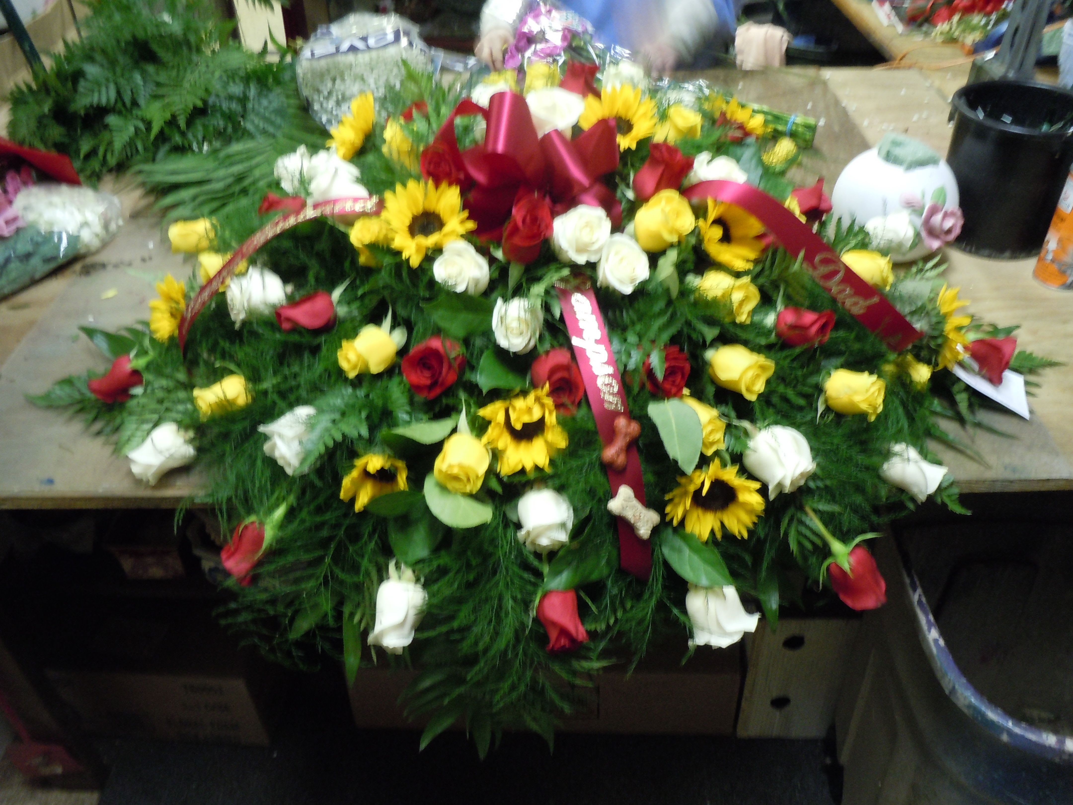 C28 Casket Spray - A mixture of white, yellow and red roses, sunflowers, greens, and baby's breath, includes bow.  Banners are $15.00   Substitutions may apply, pending flower availability.