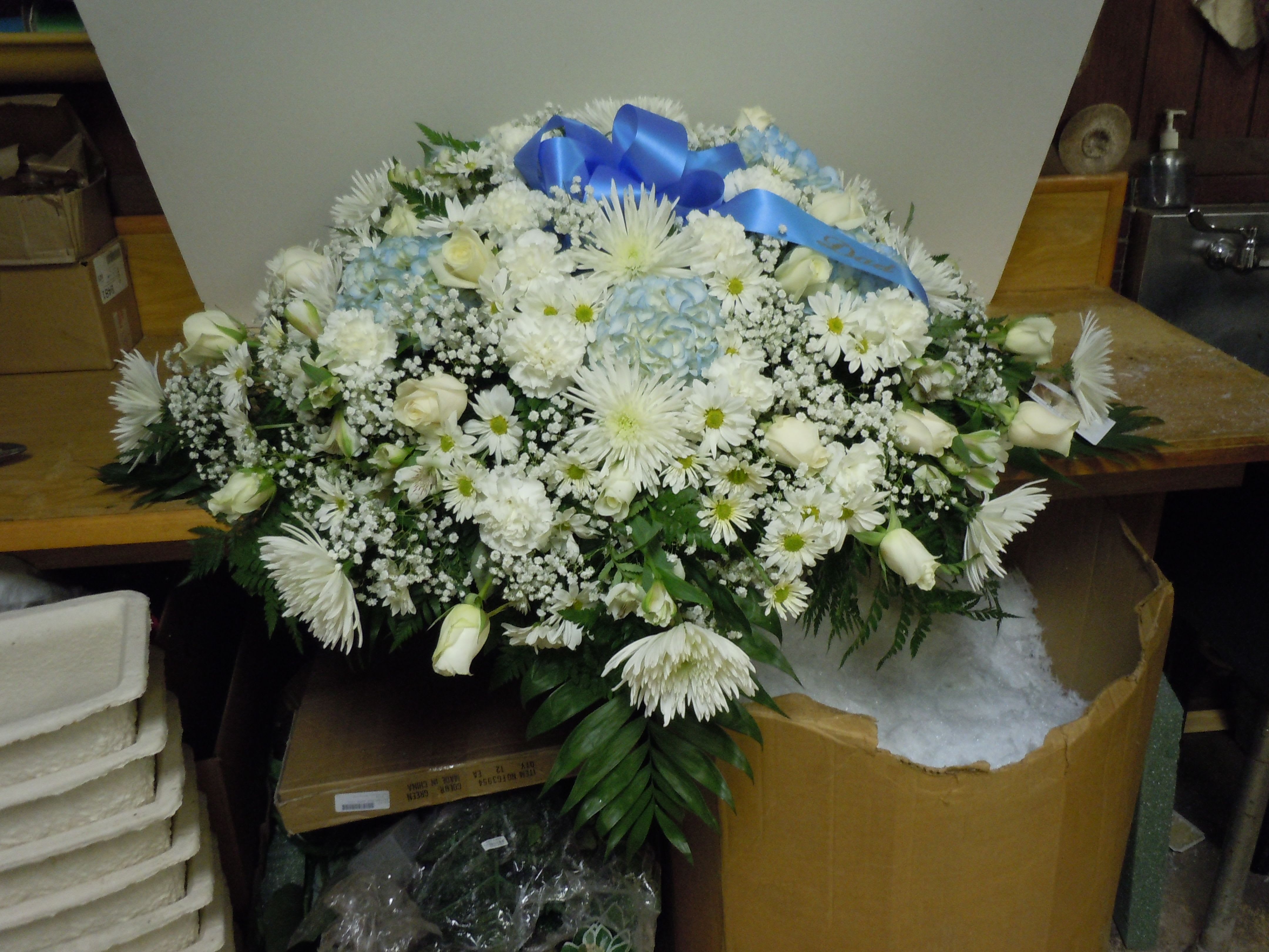 C30 Casket Spray - A mixture of white fuji mums, white roses, white carnations, white daisies, light blue hydrangeas, white alstromeria, greens, and baby's breath, includes bow.  Banners are $15.00 +    Substitutions may apply, pending flower availability.