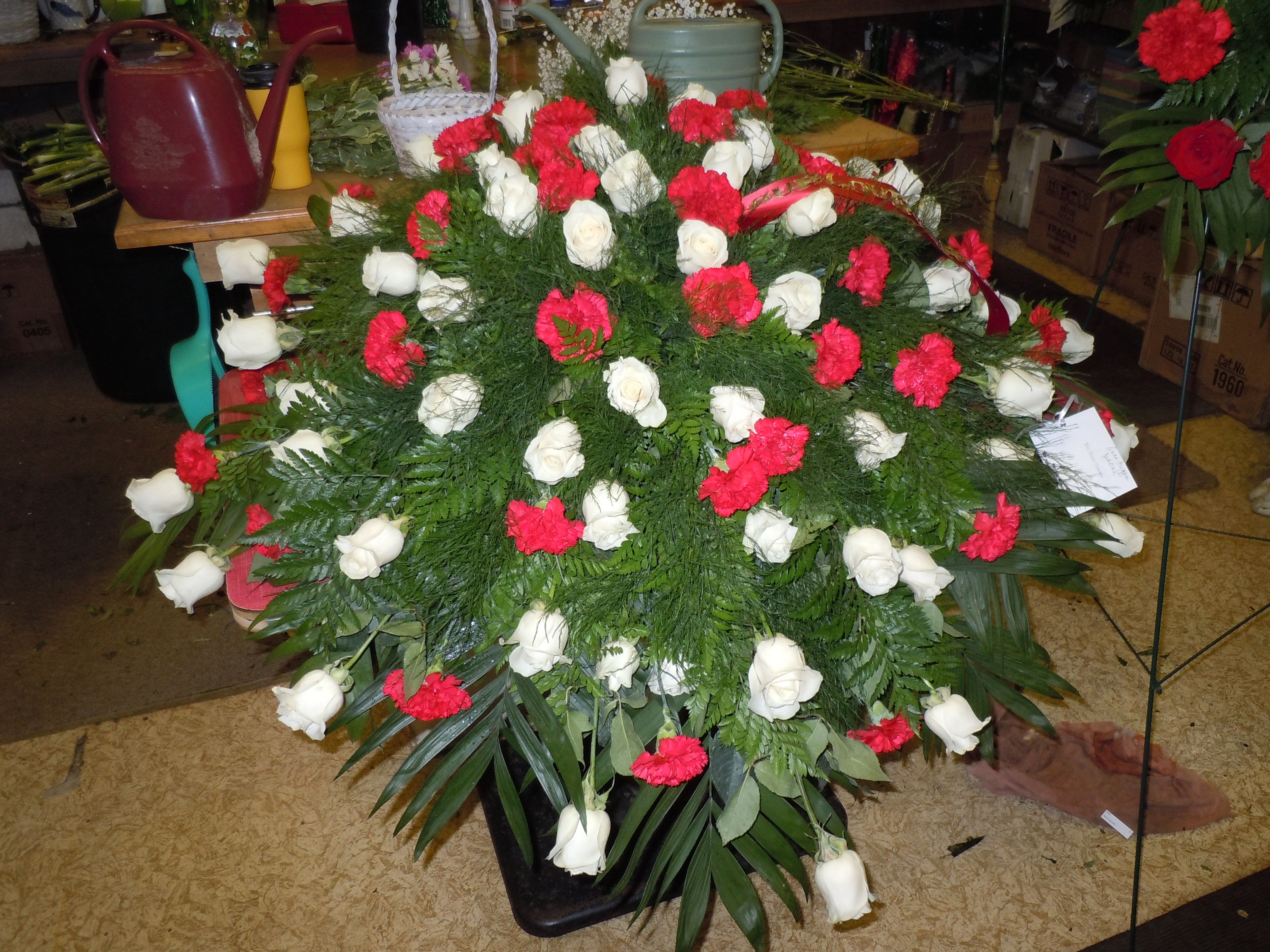 C31 Casket Spray - Extended size casket spray -   A mixture of white  roses, pink carnations, red carnations greens, and baby's breath, includes bow.  Banners are $15.00 +   Substitutions may apply, pending flower availability.
