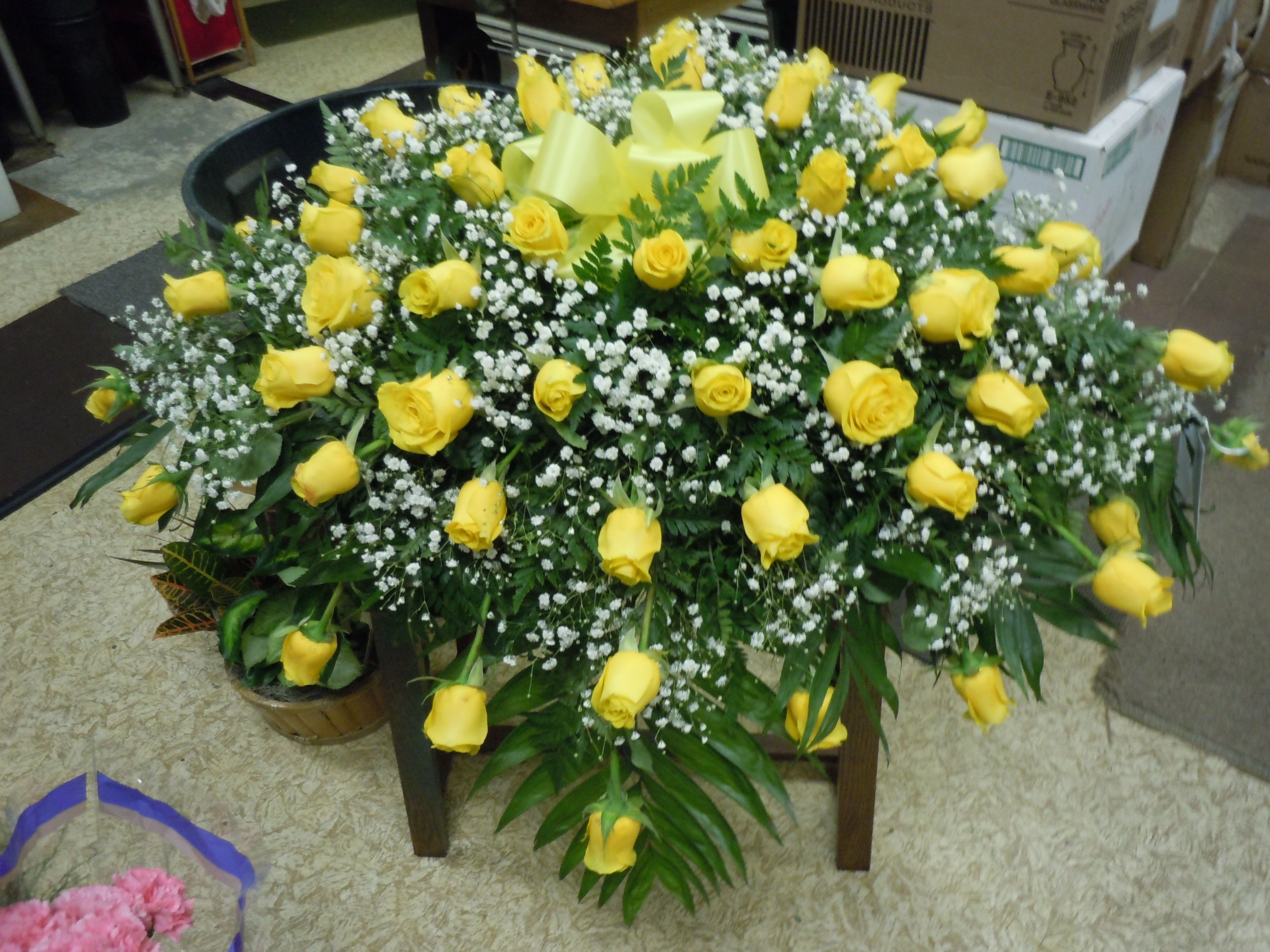 C32 Casket Spray - Extended length casket spray -   A mixture of yellow roses,  greens, and baby's breath, includes bow.  Banners are $15.00 +    Substitutions may apply, pending flower availability.