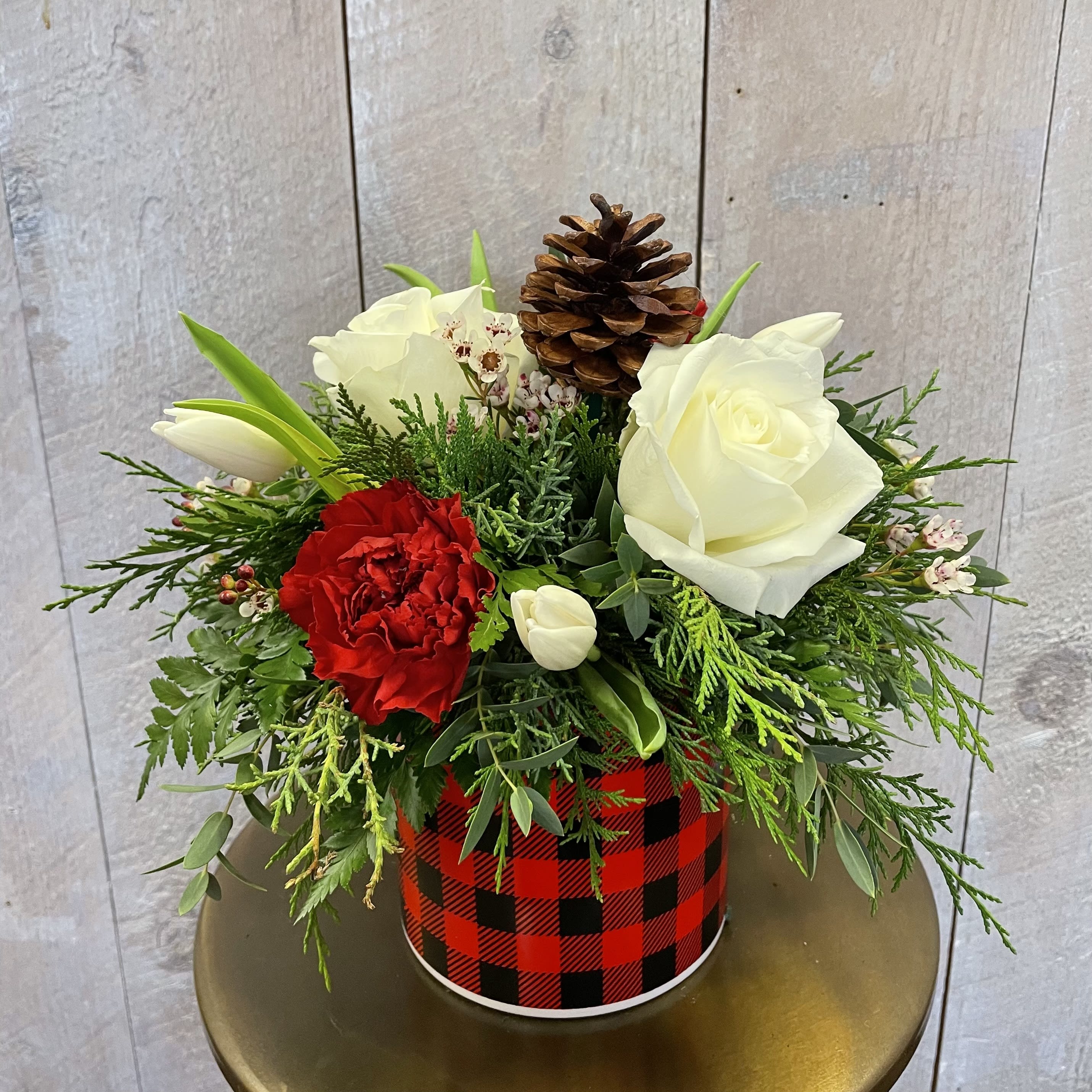 Festive Florals - A festive arrangement in a round buffalo check container featuring a wintry mix of roses, tulips, carnations, waxflower, and a pinecone on mixed holiday greens!