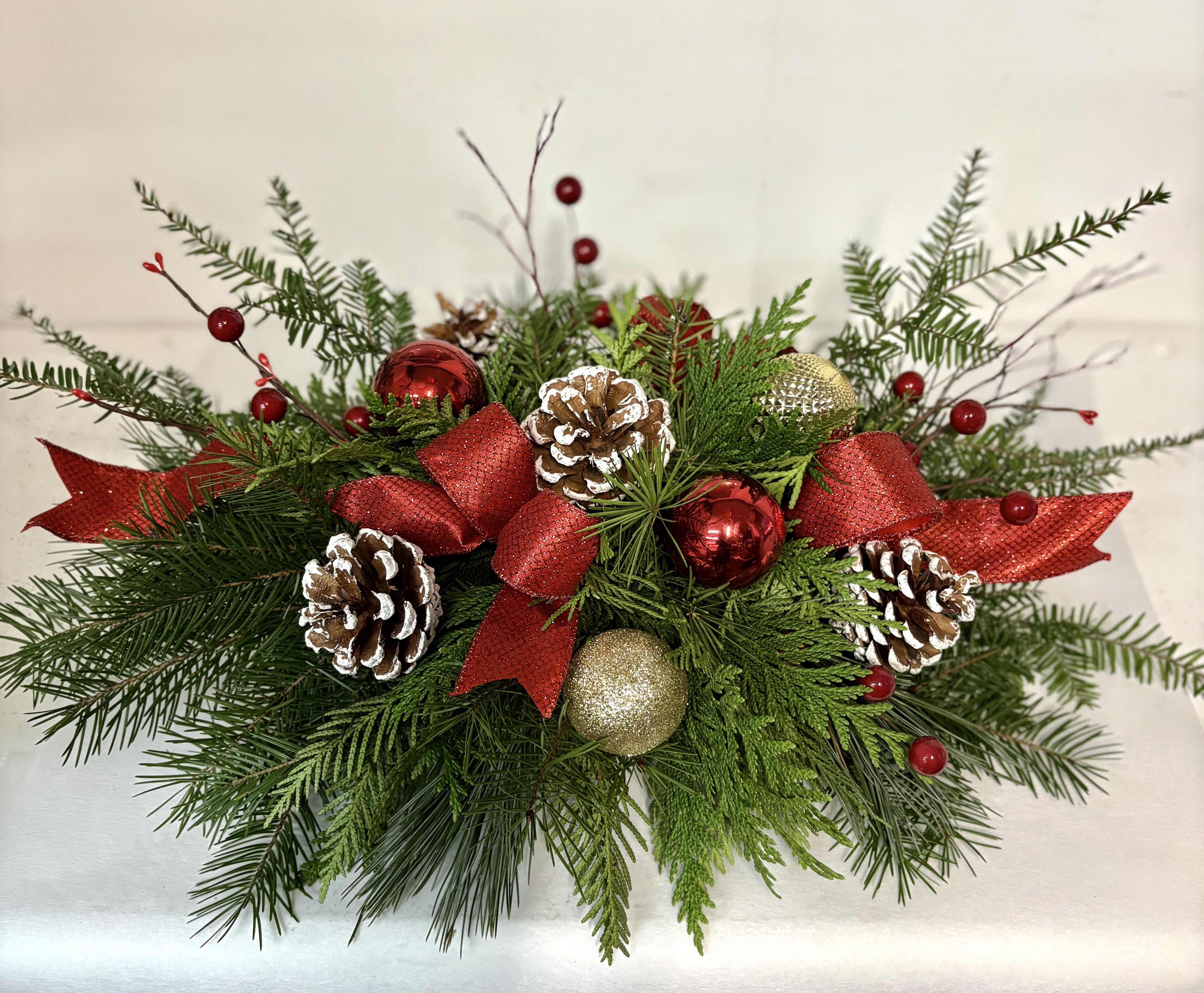 Red and Gold Cheer - This is a smaller table center with cones, berries, baubles, and fresh winter greens  there is no flowers in this design.