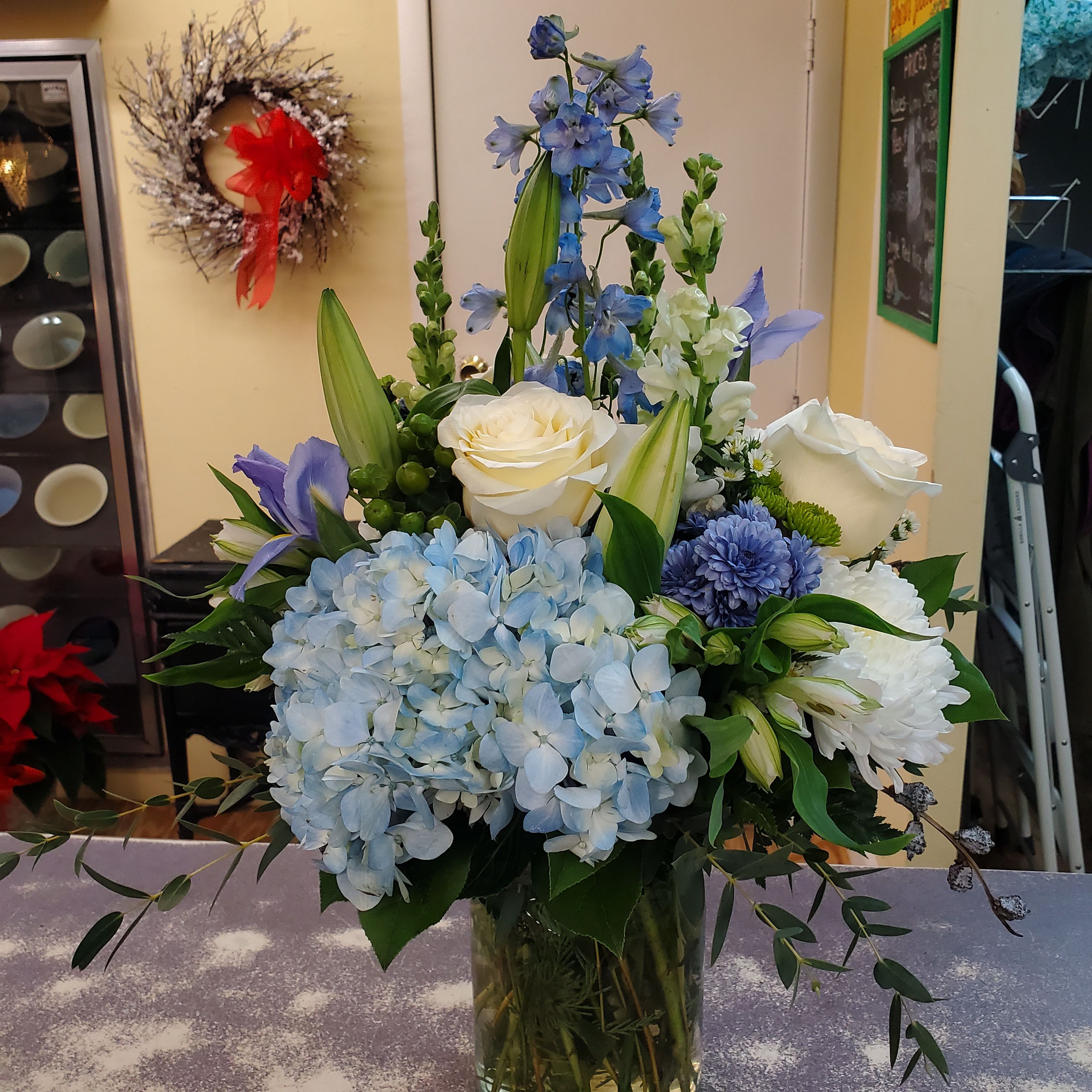  Blue Skies Bouquet  - Arrangement designed in a clear glass  container with assorted blues and white flowers accented with assorted natural greens. 
