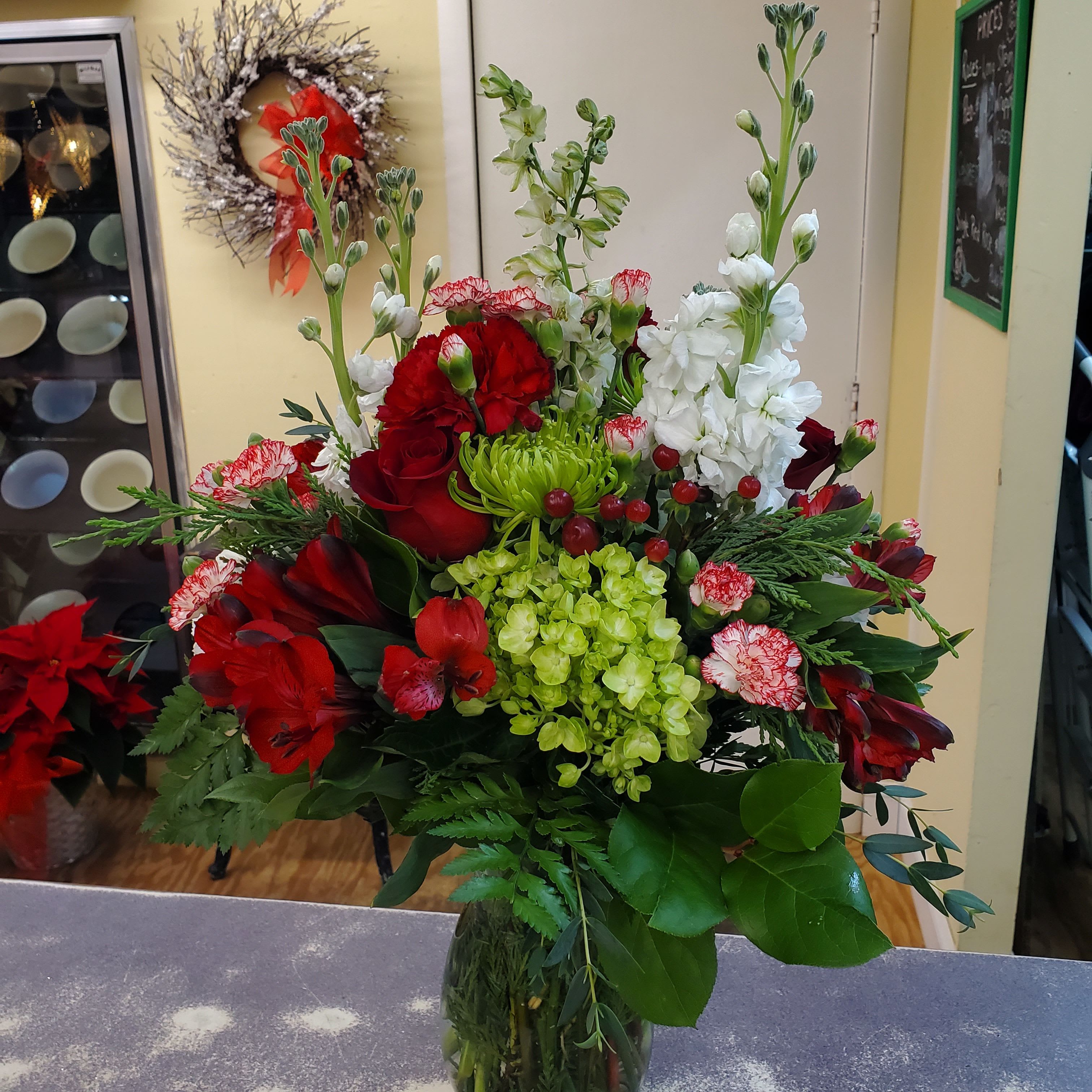 Joyful Christmas  - Seasonal flowers and assorted winter greens are designed in a compact container. Accented with glass balls and pine cones. 