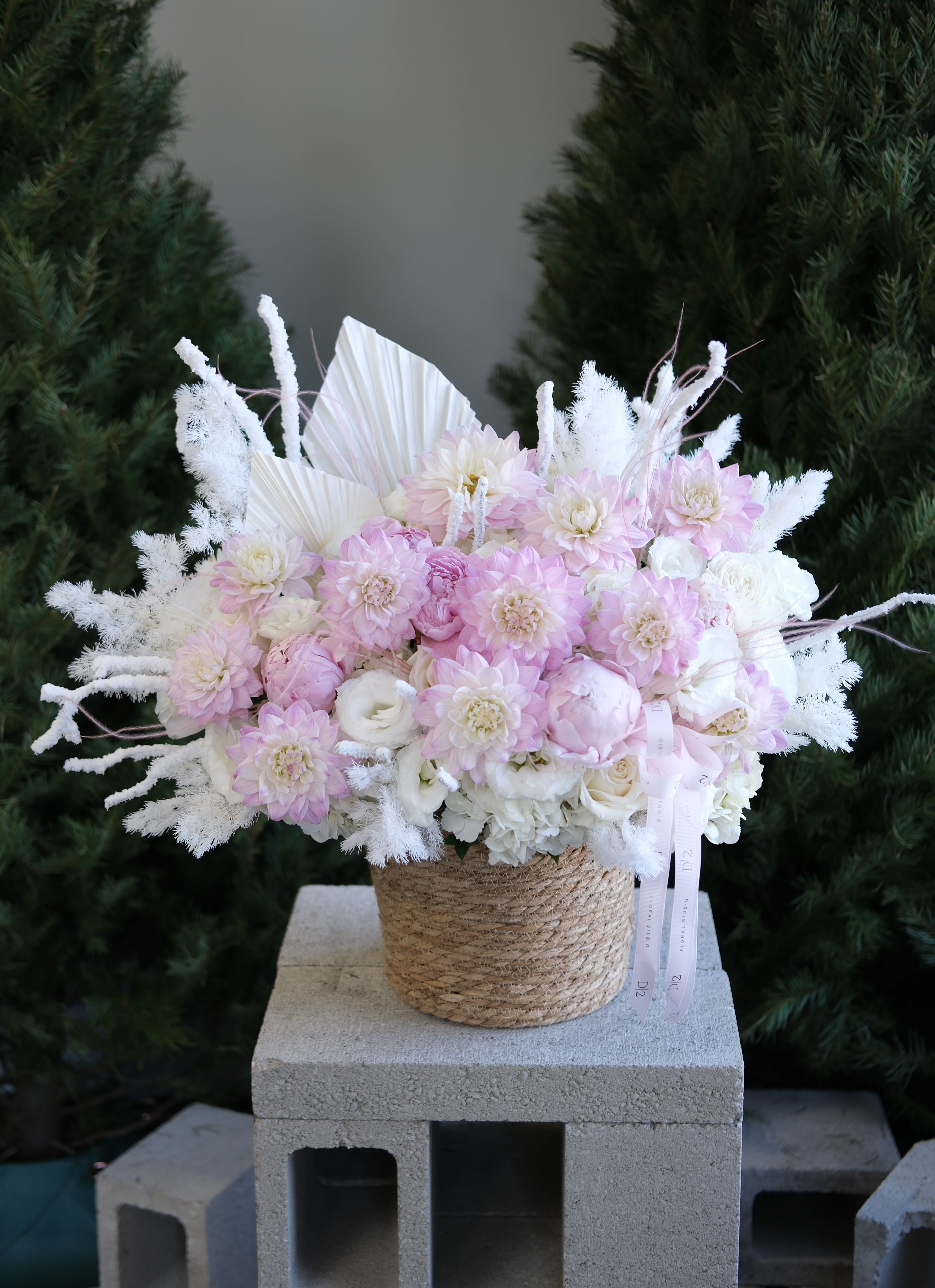 Soft Pink Winter Dream - An airy mix of blush dahlias, roses, and white accents with frosted textures, styled in a woven vessel for a dreamy winter look. 