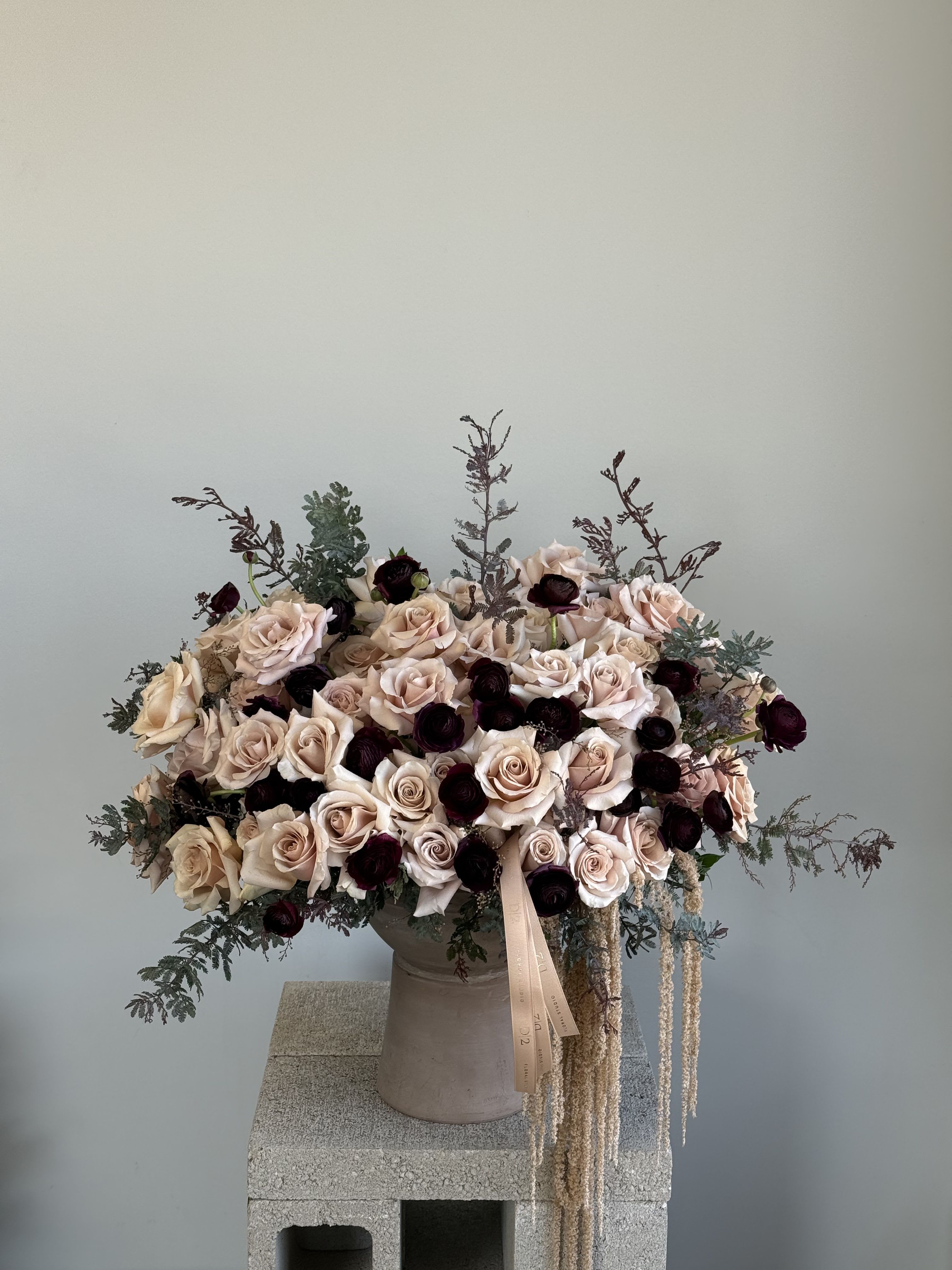 Champagne &amp; Burgundy Romance - A luxurious blend of nude roses and deep burgundy blooms with winter greenery in a tall stone vase.