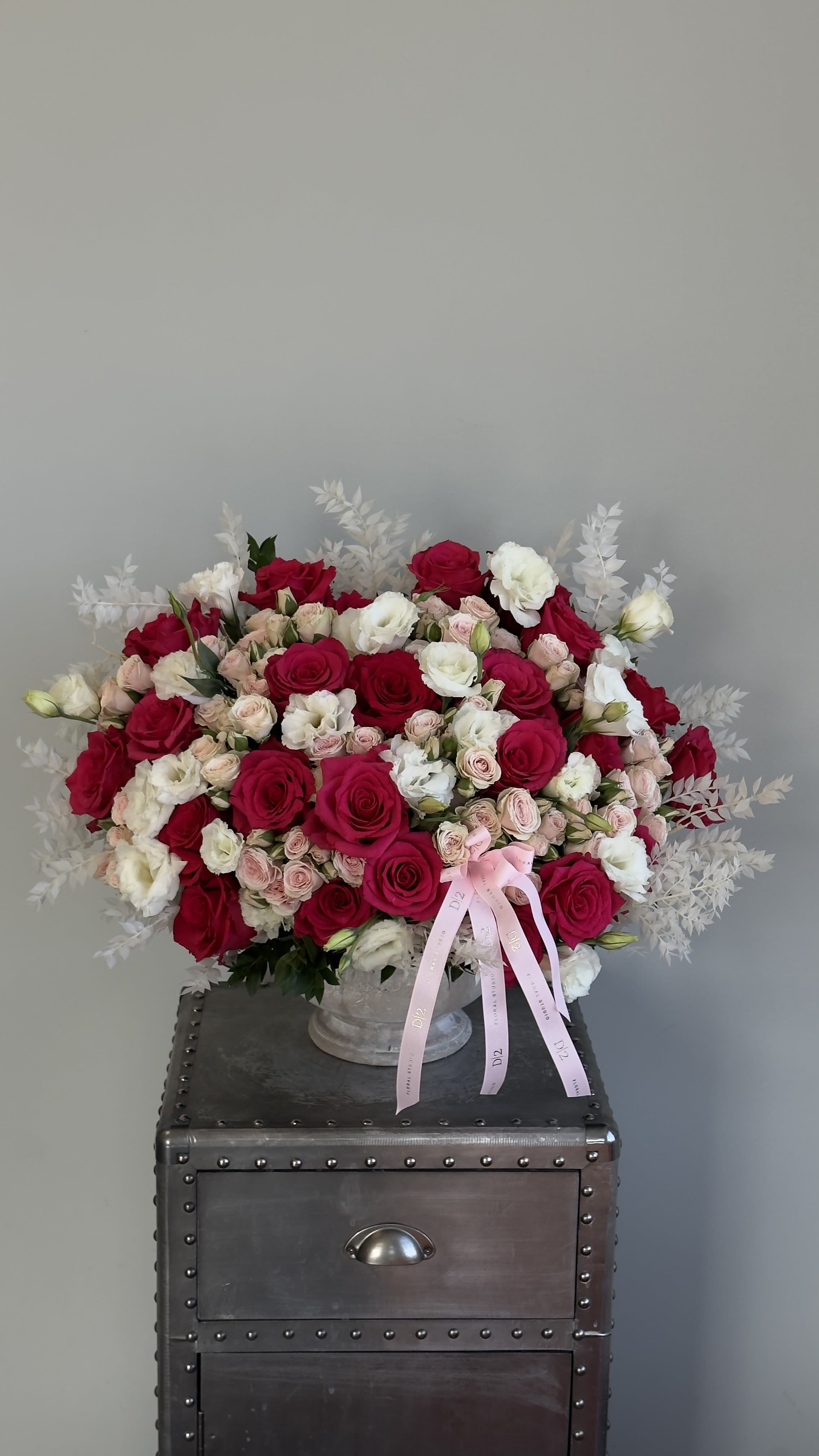 Red &amp; Pink Rose - A vibrant mix of red, blush, and white roses accented with soft white foliage, styled in a classic stone vessel.